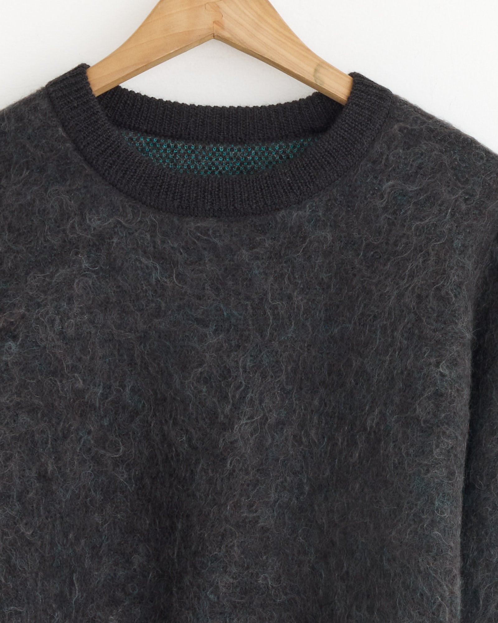 A close-up of the ssstein 1305 Sweater in Mix, featuring dark gray jacquard-knit fabric on a wooden hanger, highlighting its textured material and ribbed neckline.