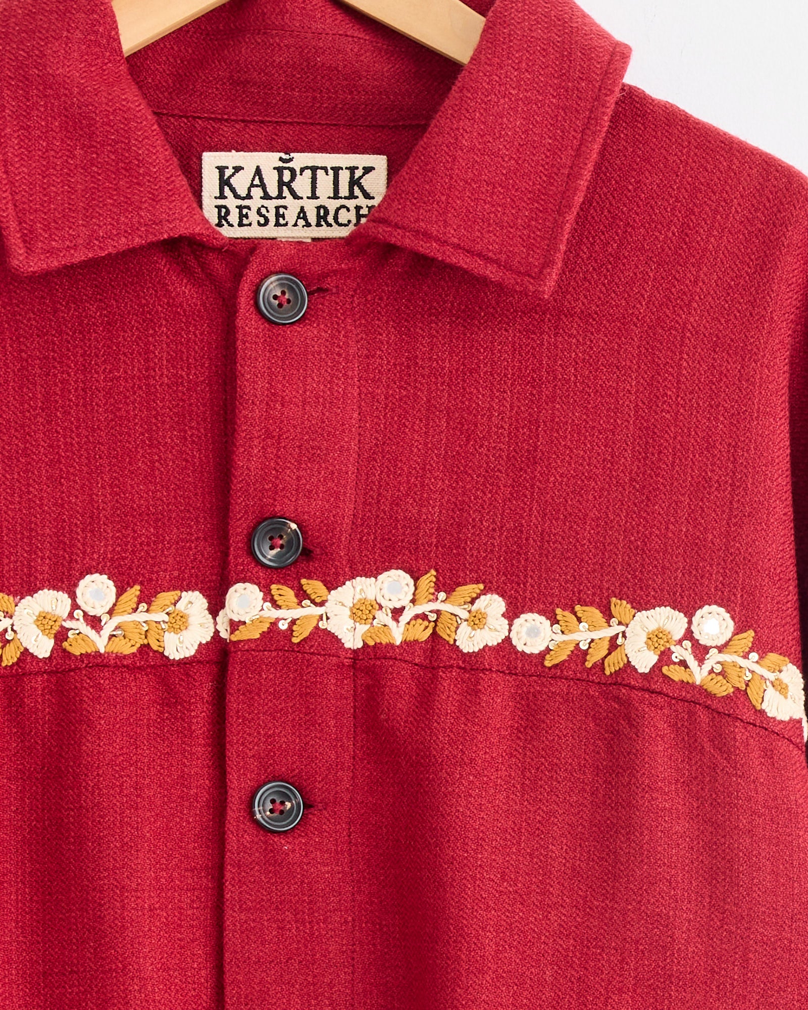 A close-up of the Rishikesh Jacket in Red/Gold/Ecru by Kartik Research, featuring black buttons and a yellow and white floral embroidered band across the chest. For fit help, check the label or use our online chat.