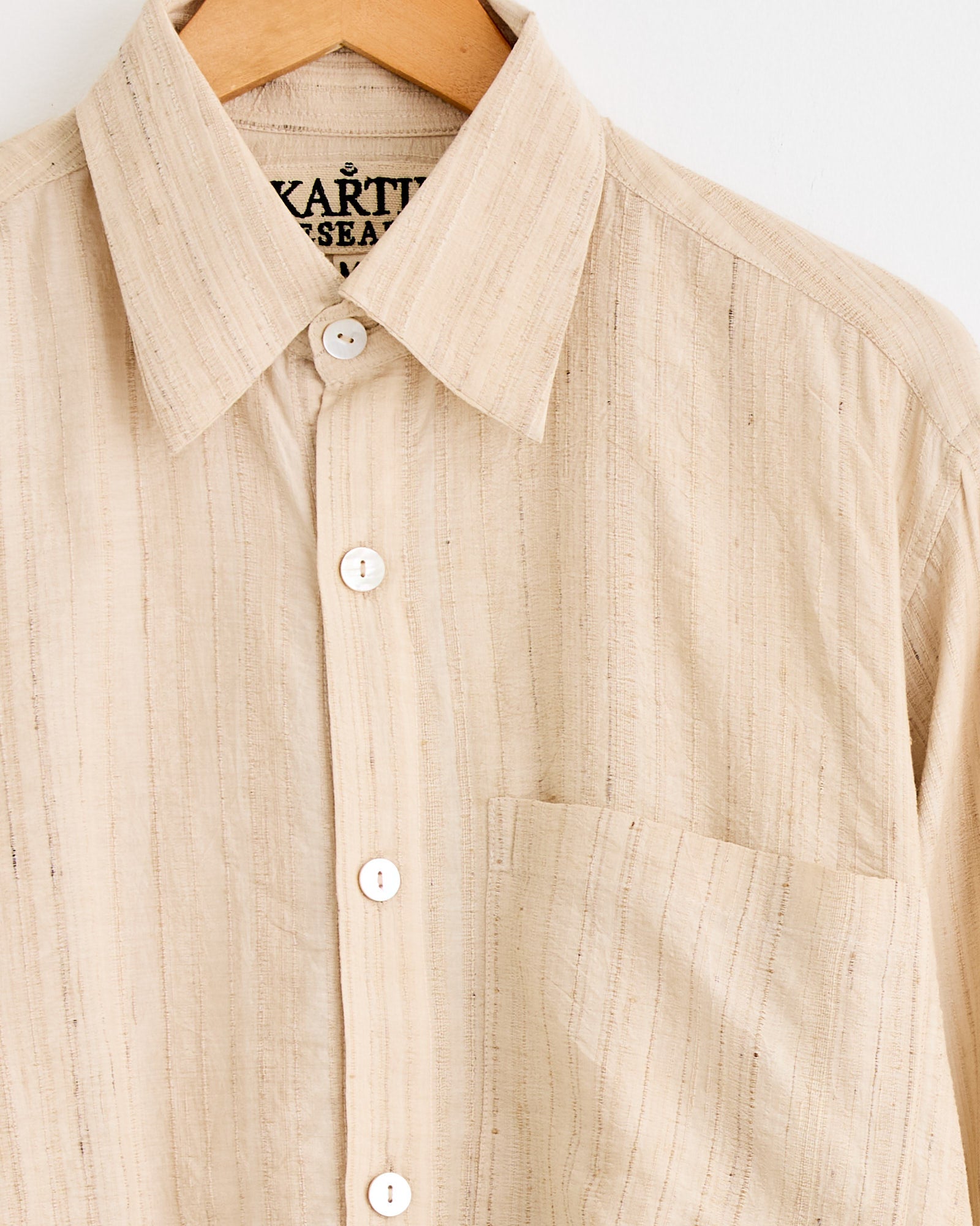 The Pataudi Shirt in Peach/Gold by Kartik Research, a handwoven silk shirt with a collar and chest pocket, hangs on a wooden hanger against a white background.