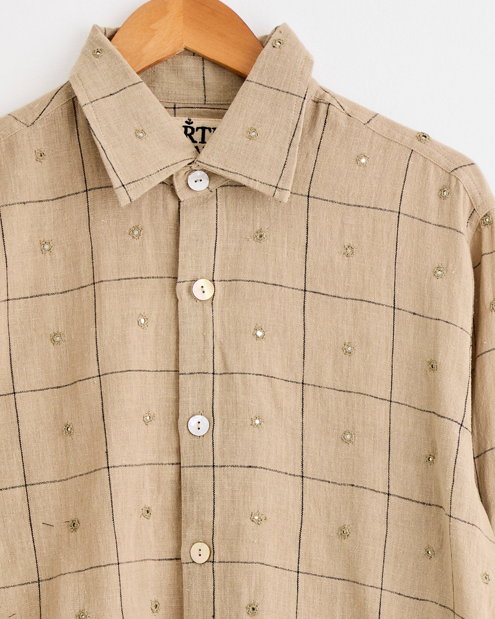 The Kartik Research Hand Embroidered Mirror Box Shirt in Beige/Indigo features intricate embroidery and is displayed on a wooden hanger.