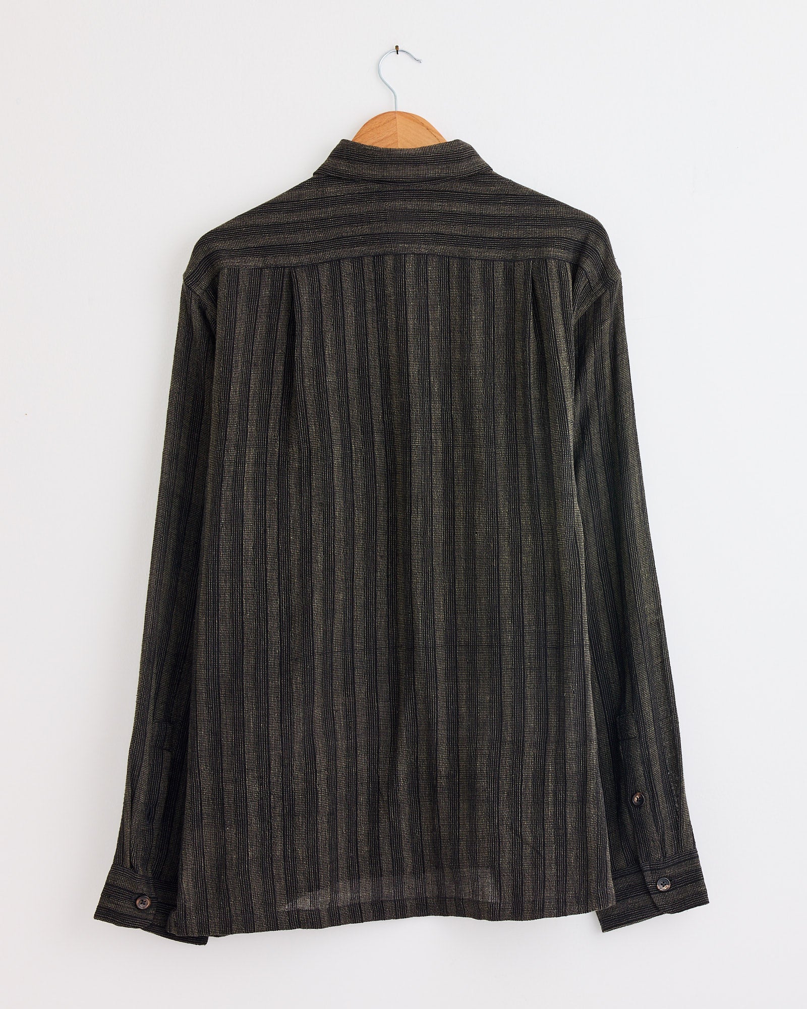 A Box Shirt in Gold/Black by Kartik Research hangs on a wooden hanger against a white wall, displayed from the back.