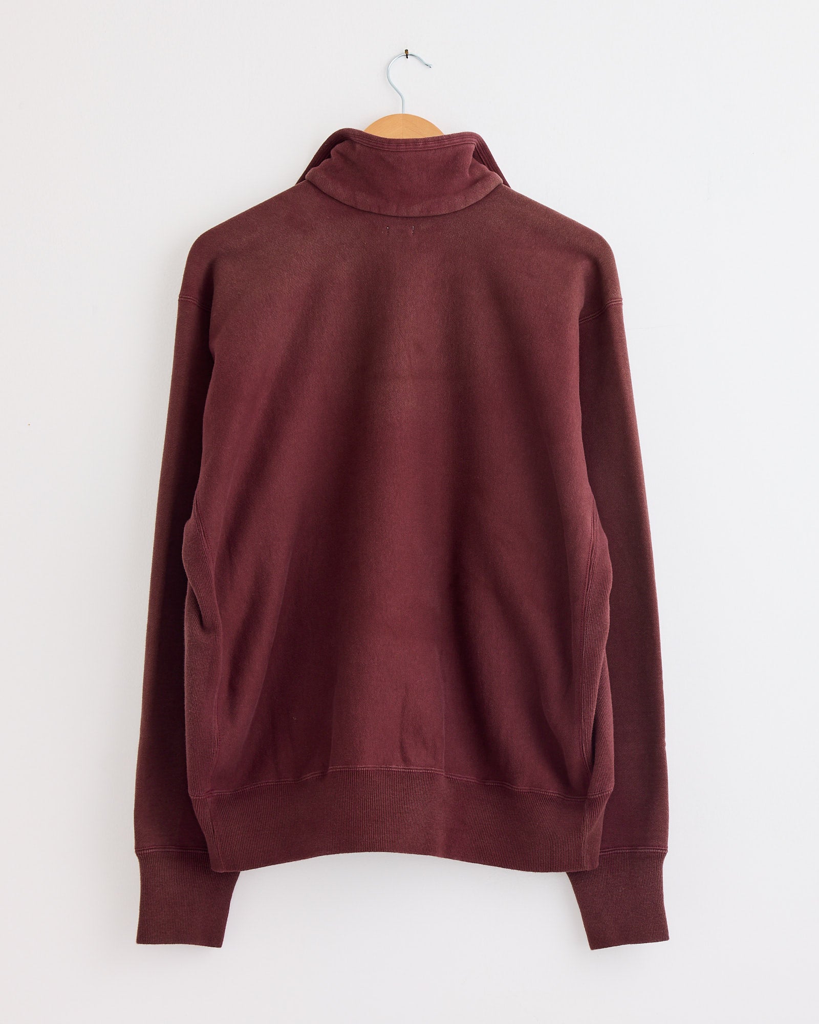 The Vintage Half Zip Sweatshirt in Burgundy by A.PRESSE is shown from the back on a hanger against a white wall. For questions about fit or sizing, please reach out via our online chat.