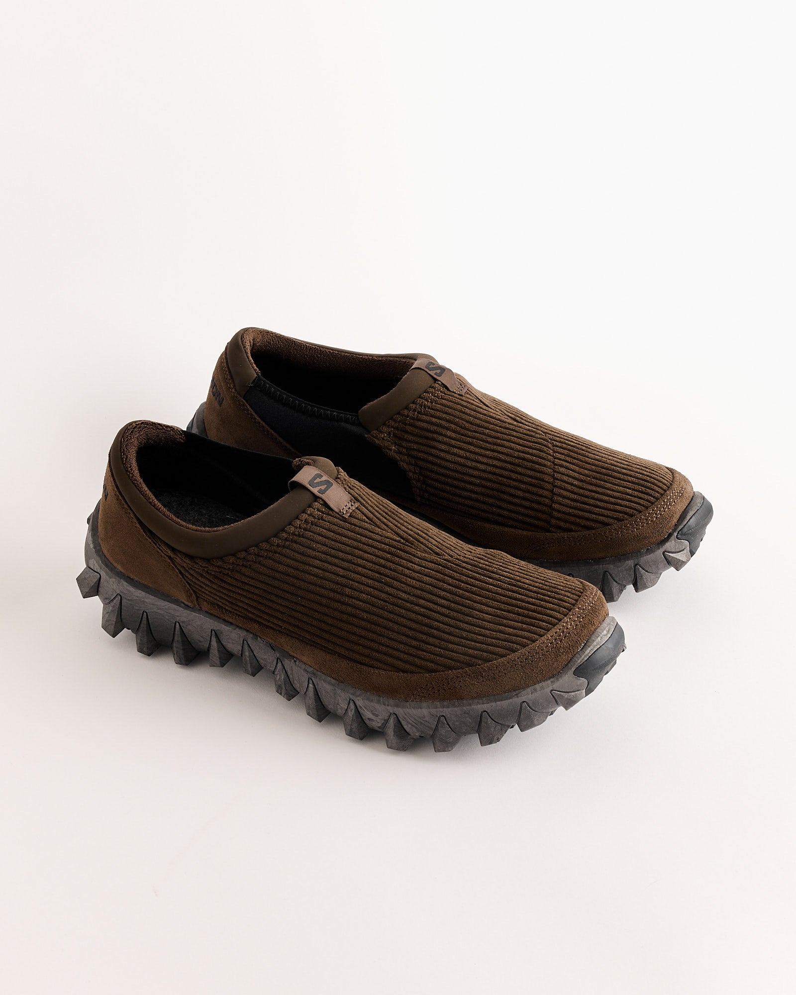 A pair of Salomon SNOWCLOG CORDUROY slip-on shoes in Diciso/Black, featuring textured corduroy uppers and thick, rugged black soles with deep treads, displayed on a white background.