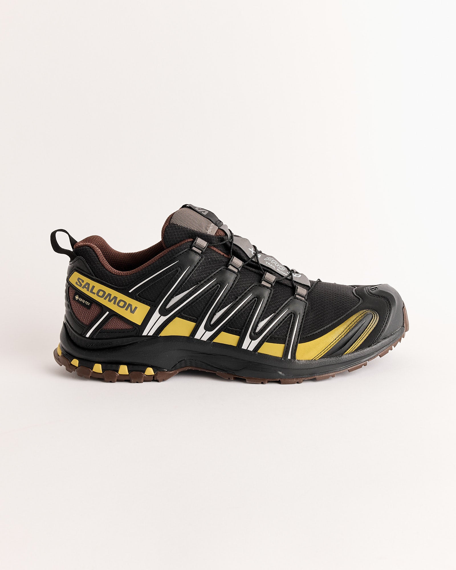 The Salomon XA PRO 3D GTX Sneakers in Black/Crgree/Roast feature a rugged sole, mesh upper, and quick-lace system. Waterproof and designed for tough terrain, these trail shoes are shown in profile against a plain white background.