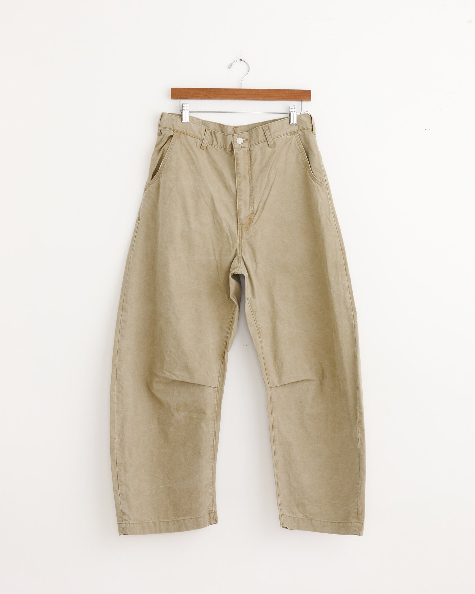 The Barrel Leg Pant in Beige from Comme Des Garçons Homme displayed on a hanger.