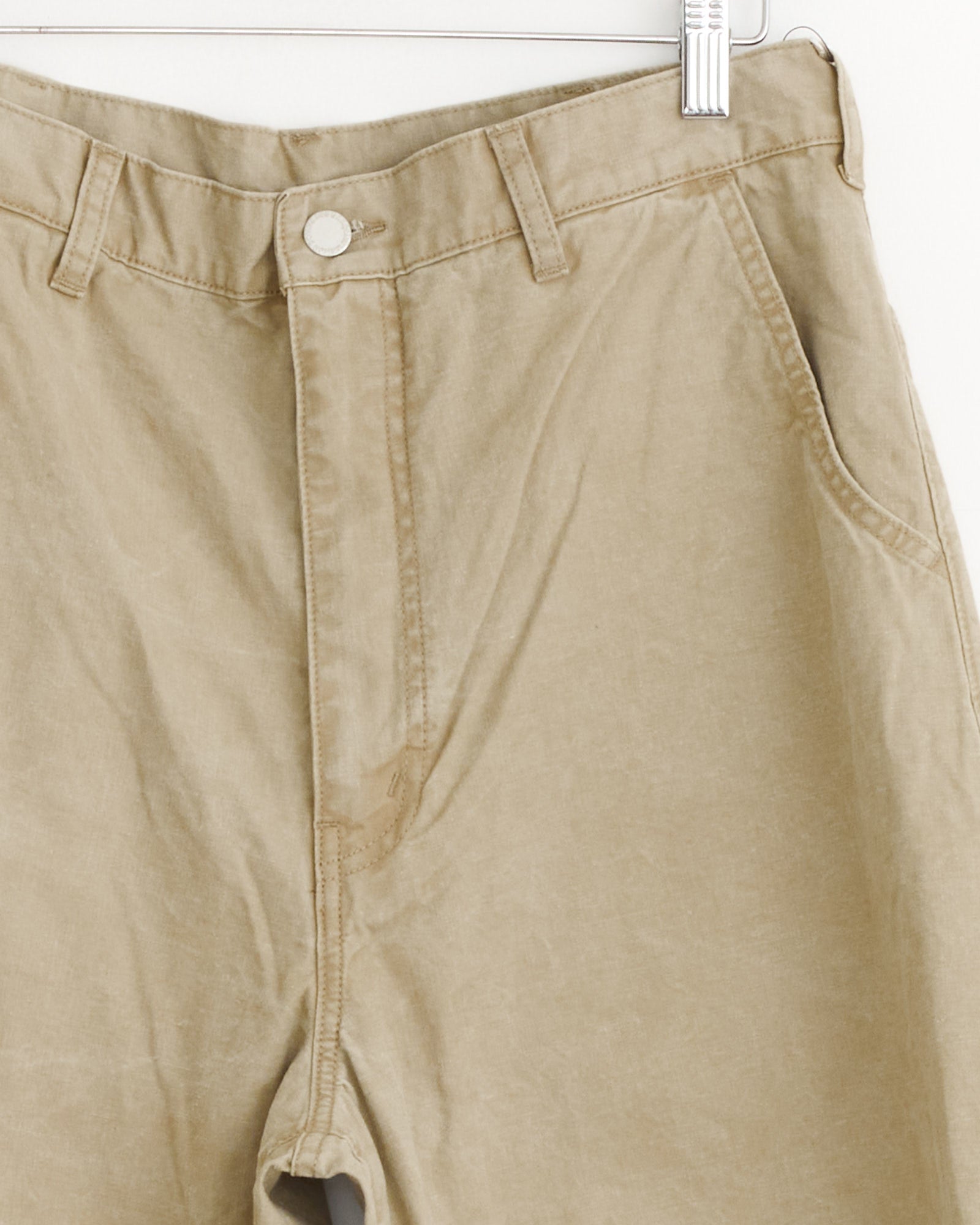 A close-up of the Beige Barrel Leg Pant by Comme Des Garçons Homme shows a visible stain near the zipper and side pockets, hanging on a hanger.