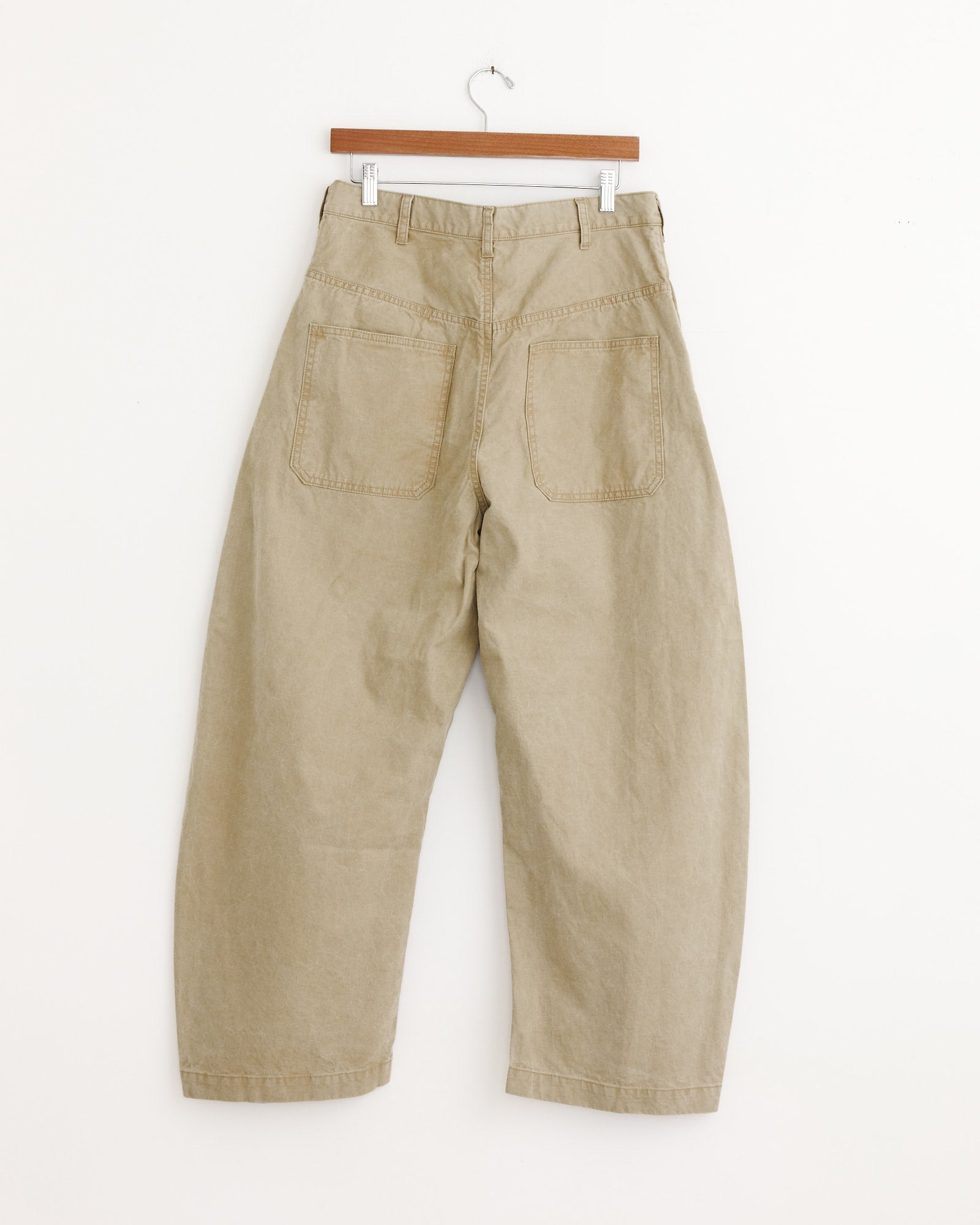 A pair of Barrel Leg Pants in beige from Comme Des Garçons Homme displayed on a hanger.