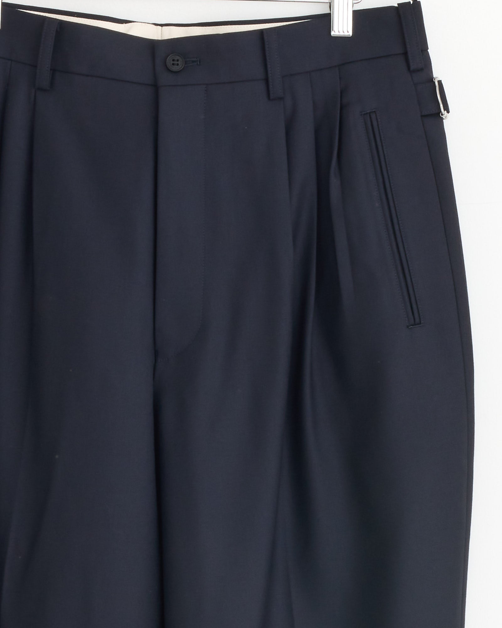 Close-up of the upper part of the Buckle Pant in Navy by Comme Des Garçons Homme, showing tailored fit, button closure, belt loops, pleats, and a right-side vertical slit pocket.