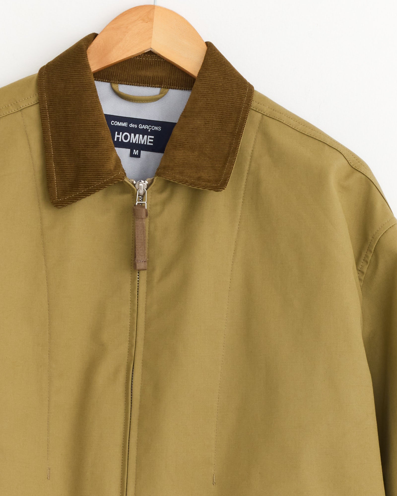 A weather resistant Triple Layer Jacket in Beige by Comme Des Garçons Homme features a brown corduroy collar, front zipper, hanger, and an interior label reading COMME des GARÇONS HOMME M.