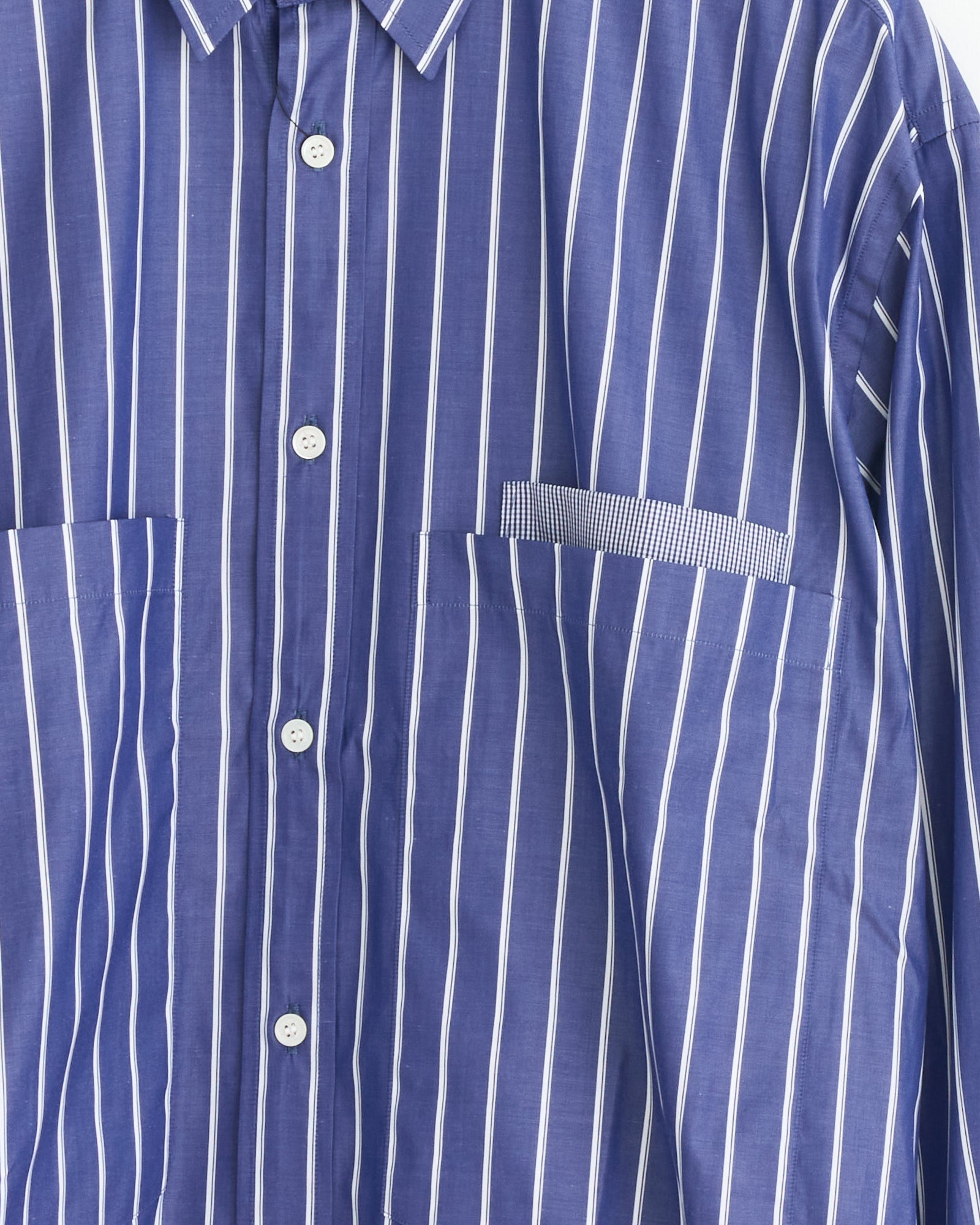 The Striped Pocket Shirt in Navy/White by Comme Des Garçons Homme features white buttons, two chest pockets, and a unique left pocket with contrasting stripe direction.