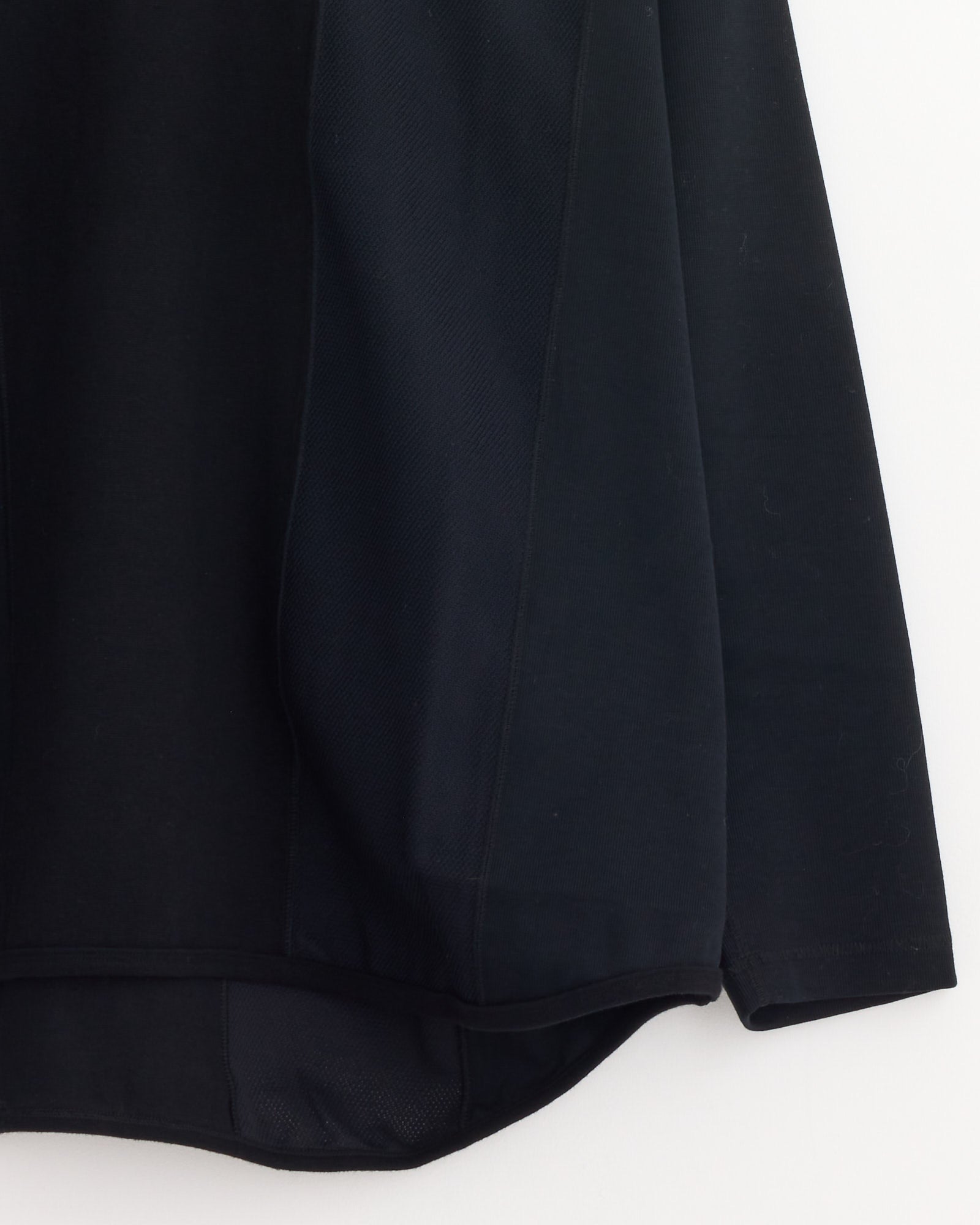 A close-up of the Comme Des Garçons Homme Panelled T-Shirt in Black Mix hangs against a white background, highlighting the lower right side, sleeve, and its curved, layered hem. Made in Japan.