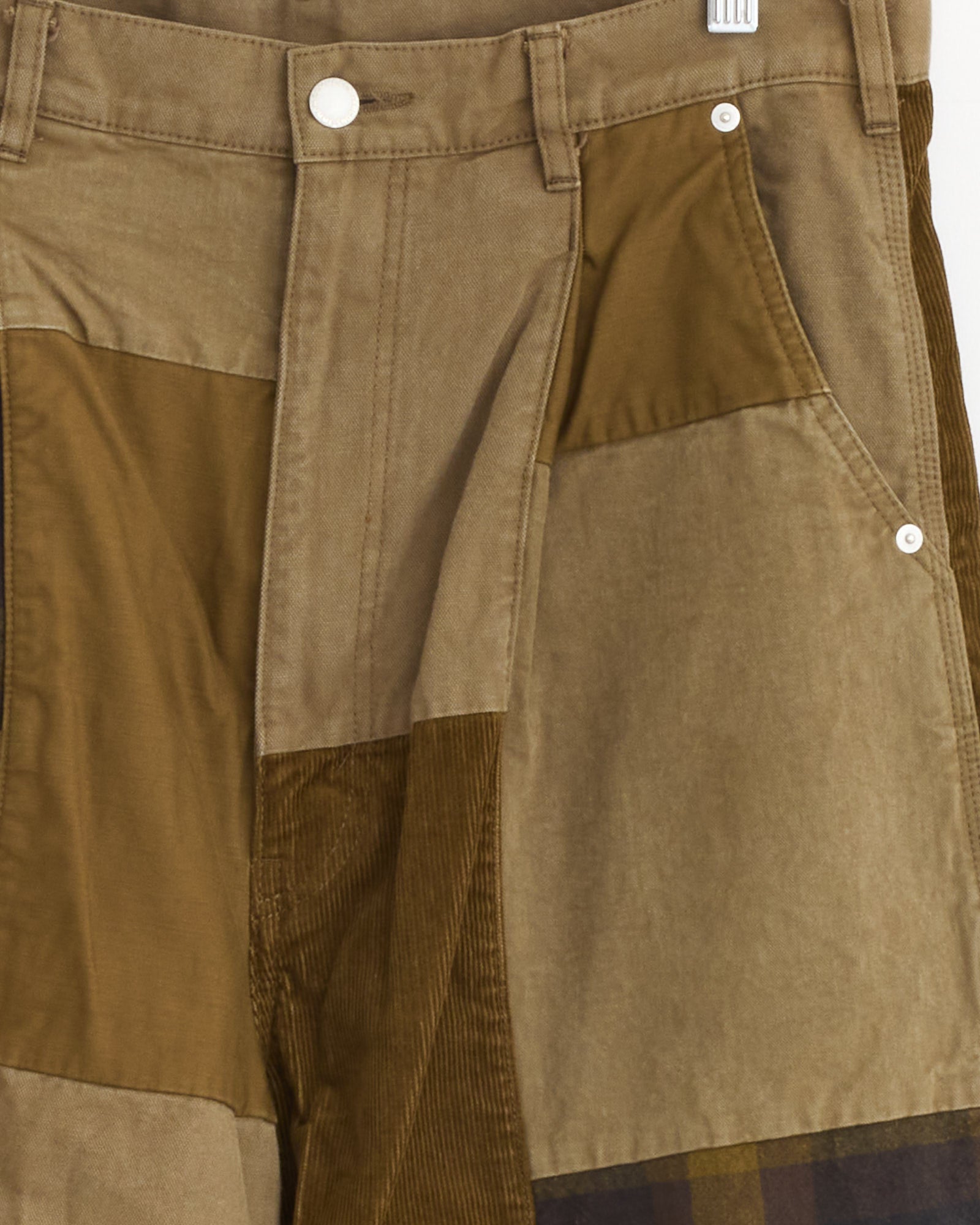 Close-up of the Comme Des Garçons Homme Patchwork Pant in Beige Mix, featuring brown and tan corduroy and plaid panels with visible seams, button, belt loops, pocket, and workwear-inspired tailoring details.
