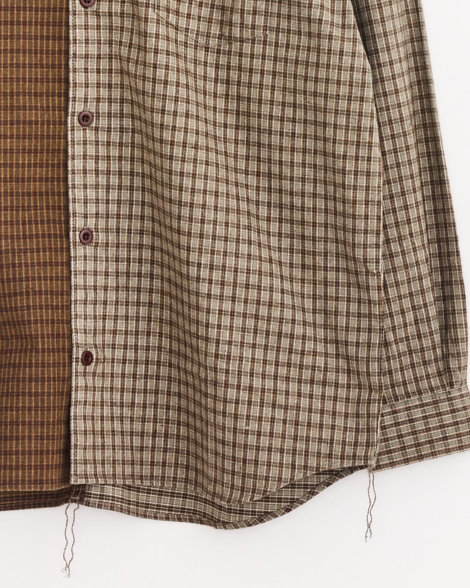 A close-up of the Double Check Shirt in Khaki/Brown by Comme Des Garçons Homme—a cotton shirt with brown and beige plaid, mismatched panels, maroon buttons, and loose threads at the frayed hem.