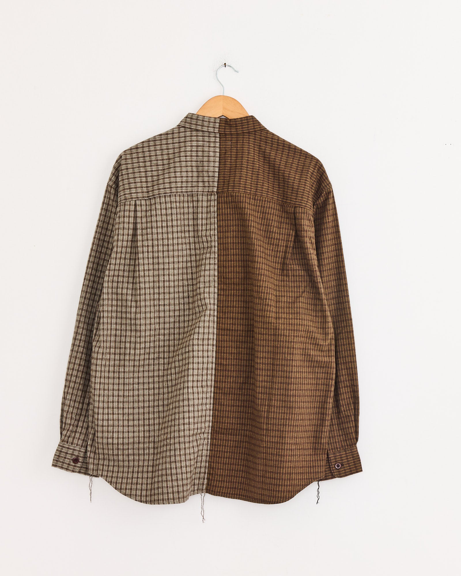 A Comme Des Garçons Homme Double Check Shirt in Khaki/Brown hangs on a wooden hanger, featuring vertically split checkered cotton: gray on the left, brown on the right.