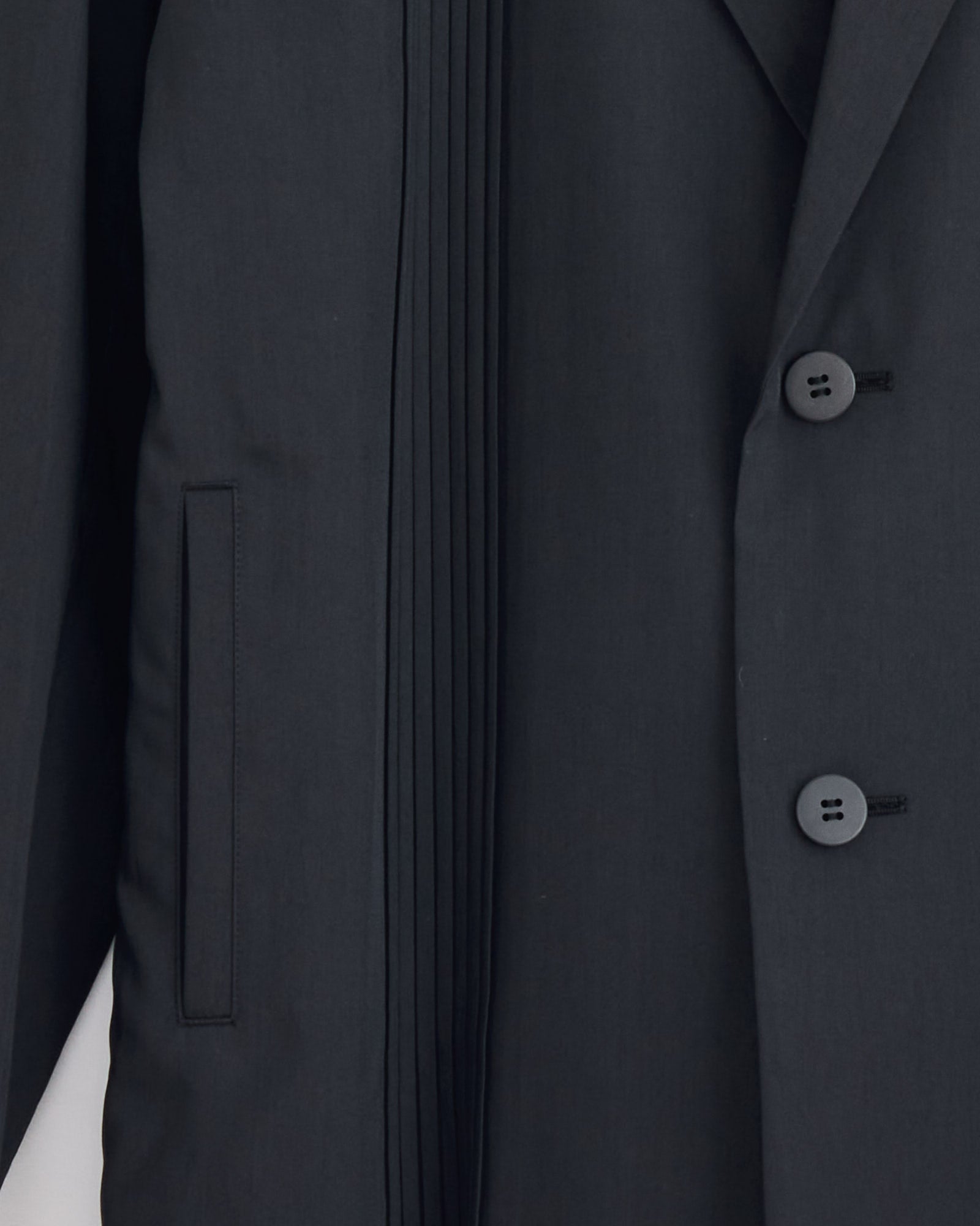 Close-up of the IM MEN Air Pleats Blazer in Black, a lightweight design with two buttons, a vertical slit pocket, and fine pleated detailing next to the lapel.