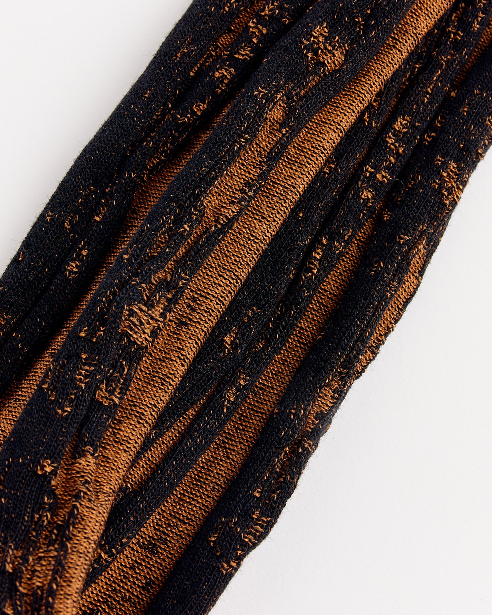 A close-up of textured fabric with alternating black and copper-brown threads, resembling the striped, slightly distressed pattern of IM MEN’s Cotton Jacquard Socks in Black.