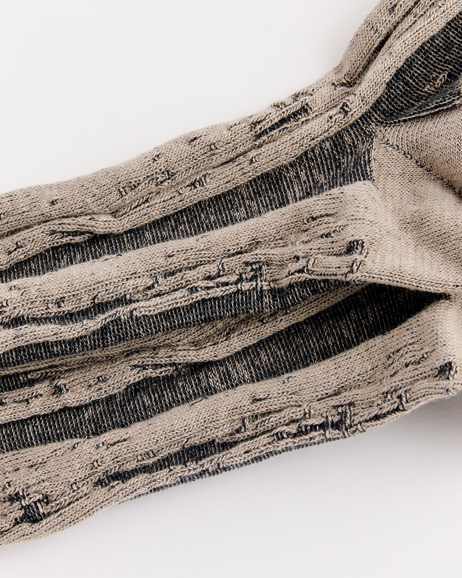 A close-up of IM MEN Cotton Jacquard Socks in Sand Beige, showing beige and black stripes with several frayed, worn-out areas and holes, highlighting significant signs of distress.