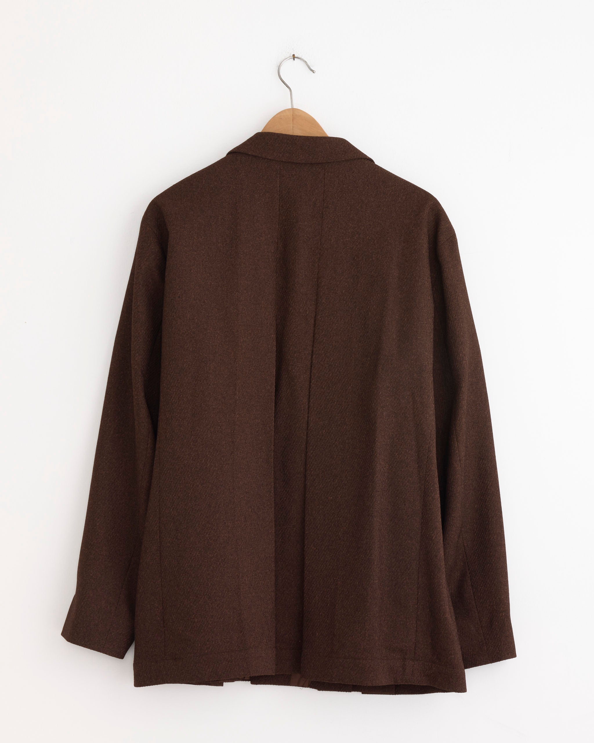 The IM MEN Wool Like Tweed Blazer in Brown hangs on a wooden hanger against a white wall, showing the back of the men's blazer.