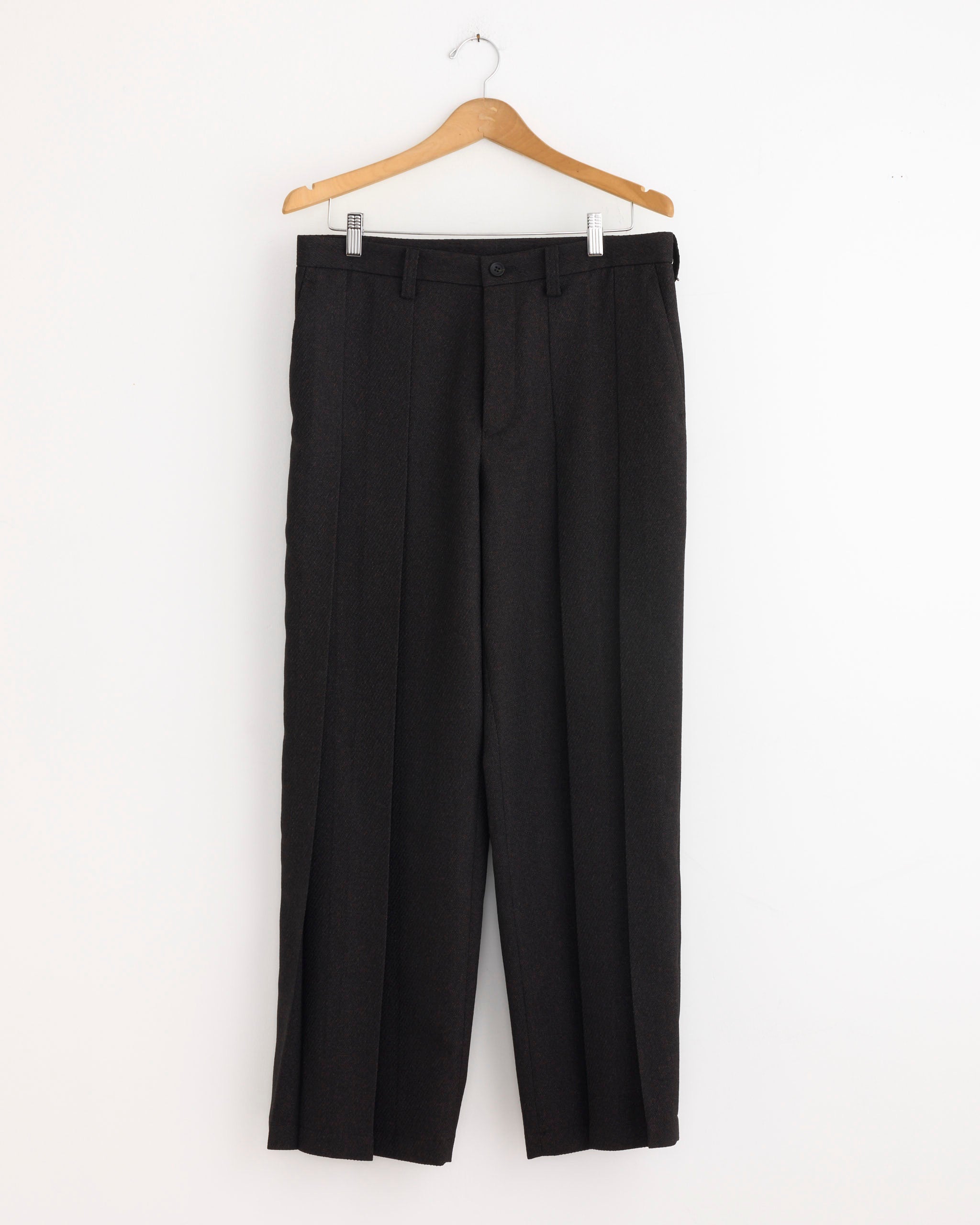 A pair of IM MEN Wool Like Tweed Pant in Dark Brown with a tapered silhouette hangs on a wooden hanger against a plain white wall.
