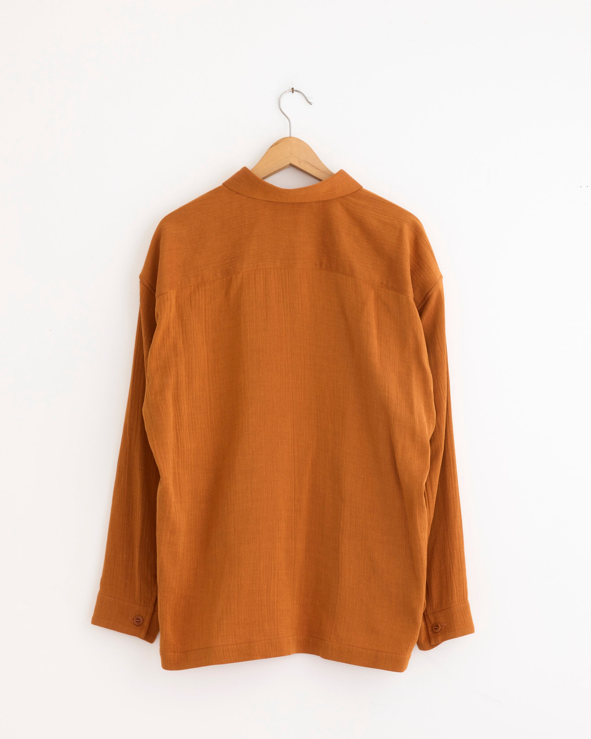The IM MEN Double Weave Crepe Shirt in Dark Orange is displayed from the back on a wooden hanger against a plain white wall—ideal for viewing fit and sizing before you buy.