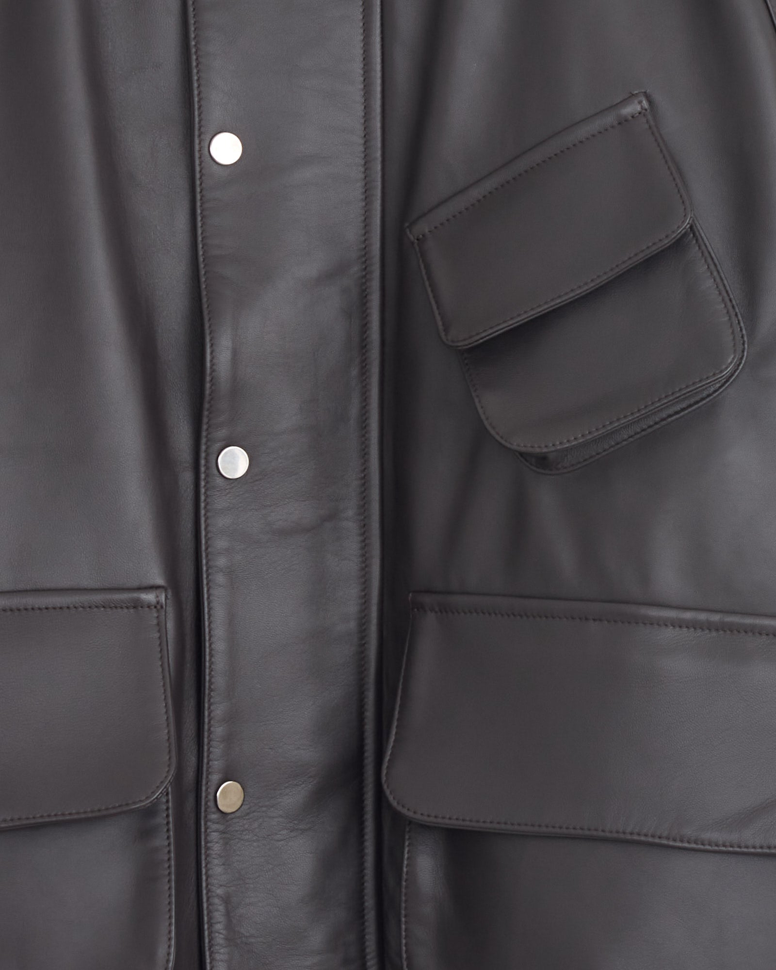 Close-up of Stoffa’s Field Blouson in Chocolate lambskin, made in Italy, showing three pockets—two large rectangular at the bottom and one angled at the upper right—with silver snap buttons down the front.
