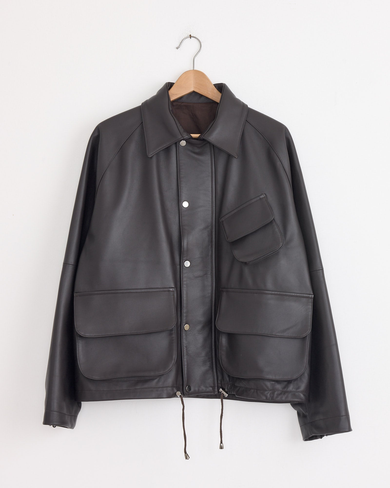 The Stoffa Field Blouson in Chocolate, crafted from lambskin with a collar, snap buttons, and three front flap pockets (including an angled chest pocket), hangs on a wooden hanger against a white background. Made expertly in Italy.