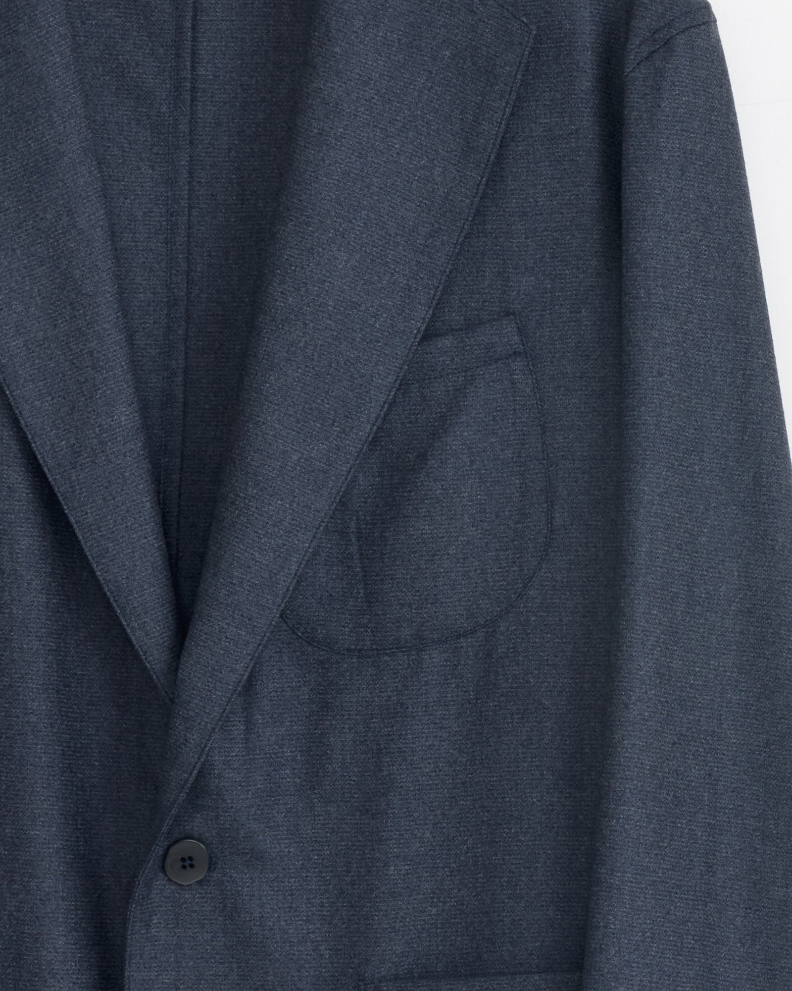Close-up of Stoffa's Single Breasted Shirt Jacket in indigo, featuring a notched lapel, single-breasted button, and chest pocket. The upper left part of the blazer is shown against a plain background. Made in Italy.