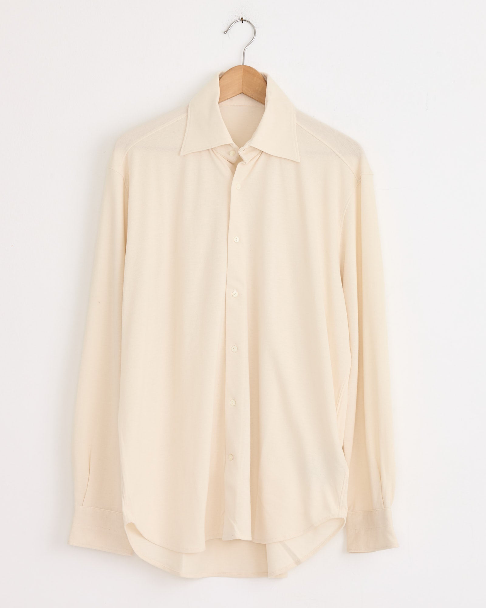 The Stoffa Spread Collar Shirt in Ivory, a long-sleeve button-up, hangs on a wooden hanger against a plain white wall.