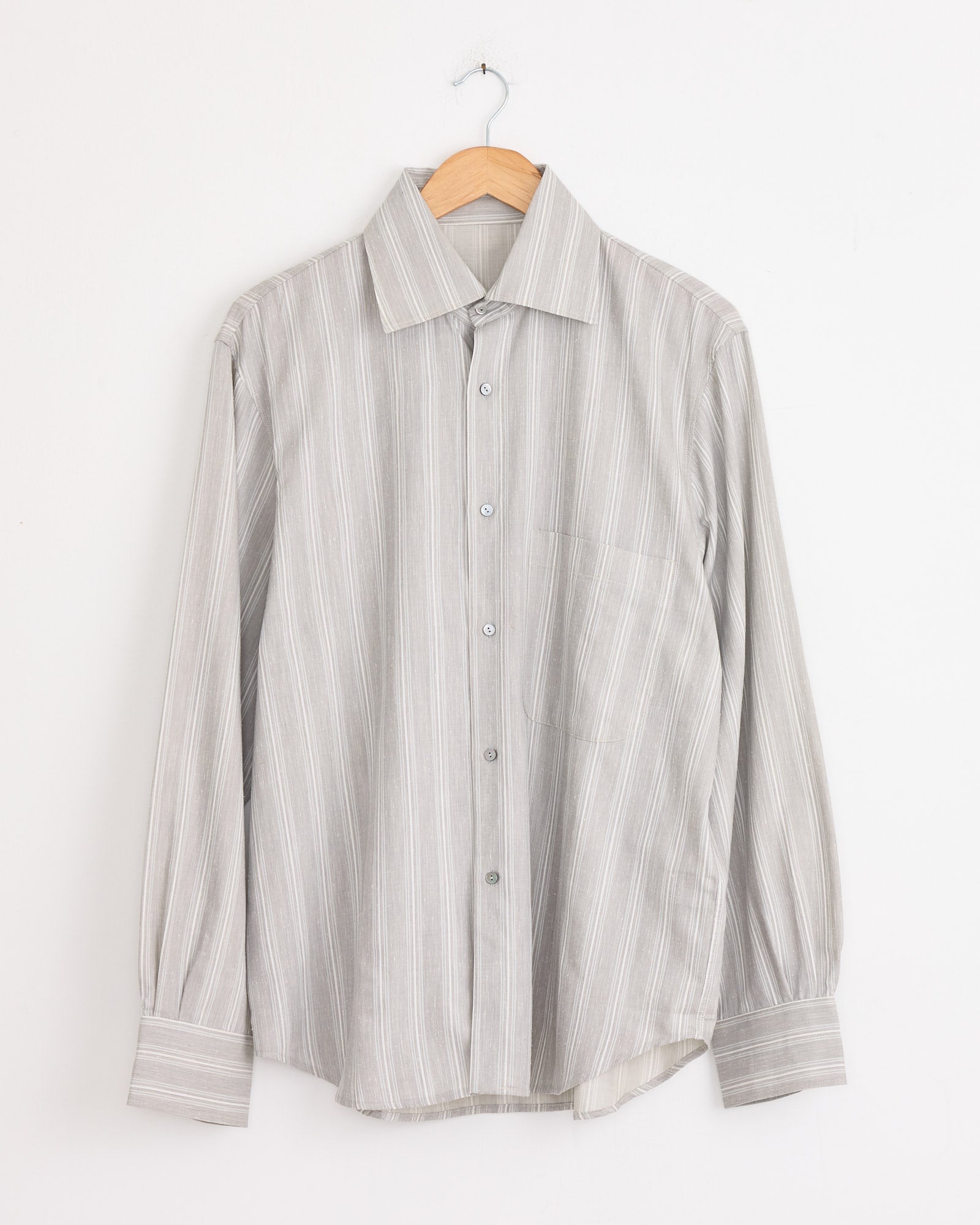 The Stoffa Spread Collar Shirt in Steel Grey/Pearl Stripe, made in Italy, with long sleeves and thin white stripes, hangs on a wooden hanger against a plain white wall.