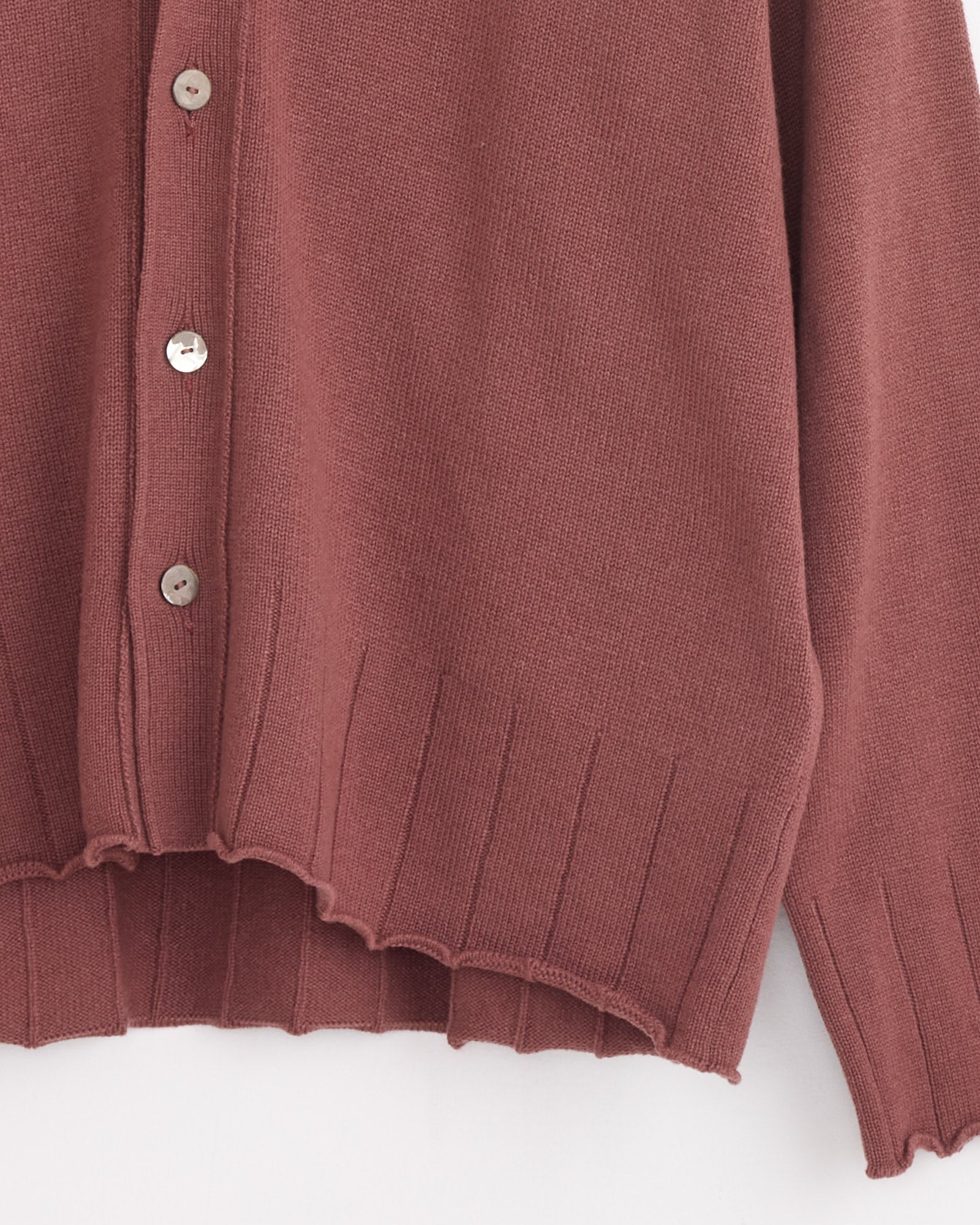 A close-up of the Stoffa Drop Shoulder Cardigan in Brick, crafted in Italy from 100% cashmere, with four silver buttons and a wide ribbed hem, set against a plain white background.