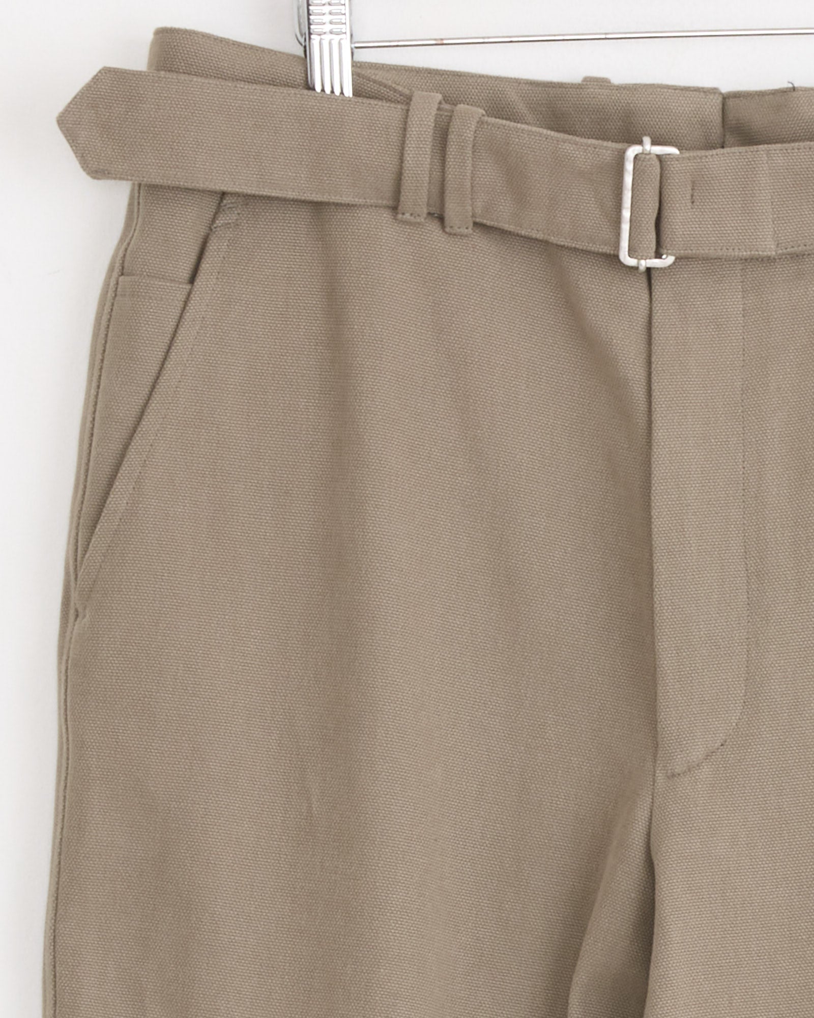 Close-up of Stoffa's Plain Front Washable Trouser in taupe, made in Italy, shown hanging on a hanger with a matching fabric belt, silver buckle, and visible side pocket.