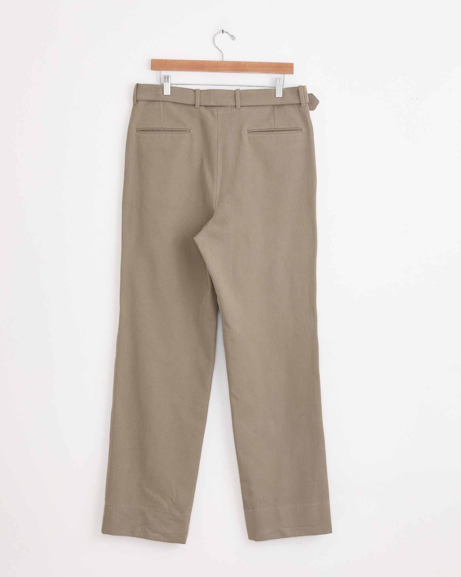 The Stoffa Plain Front Washable Trouser in Taupe, featuring belt loops and a basketweave cotton texture, is shown from the back hanging neatly on a wooden hanger against a plain white wall.