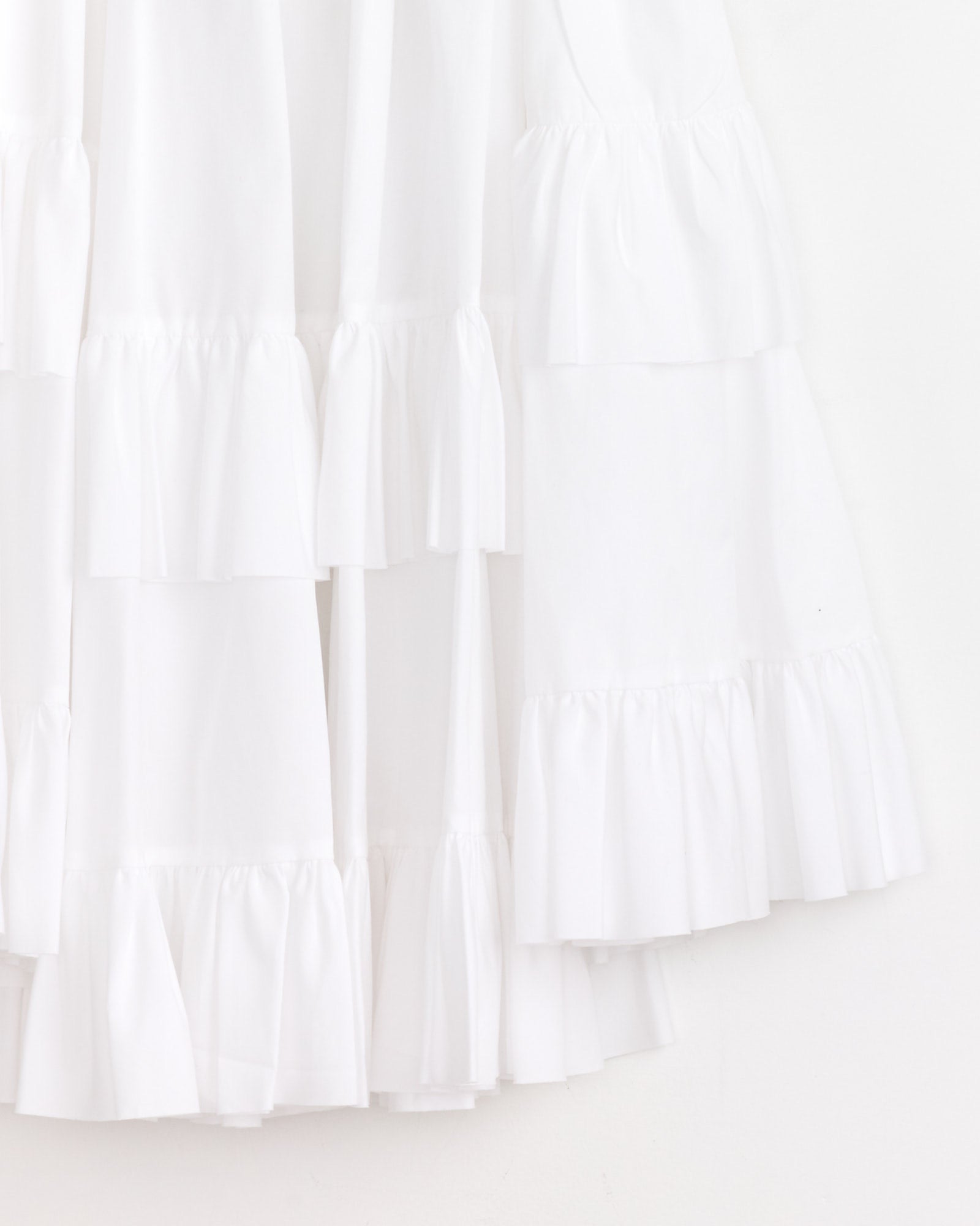 Close-up of the Comme Des Garçons Girl Ruffled Skirt in White, featuring layered ruffles and lightweight, semi-sheer fabric for a delicate, airy look. Shown hanging against a white background.