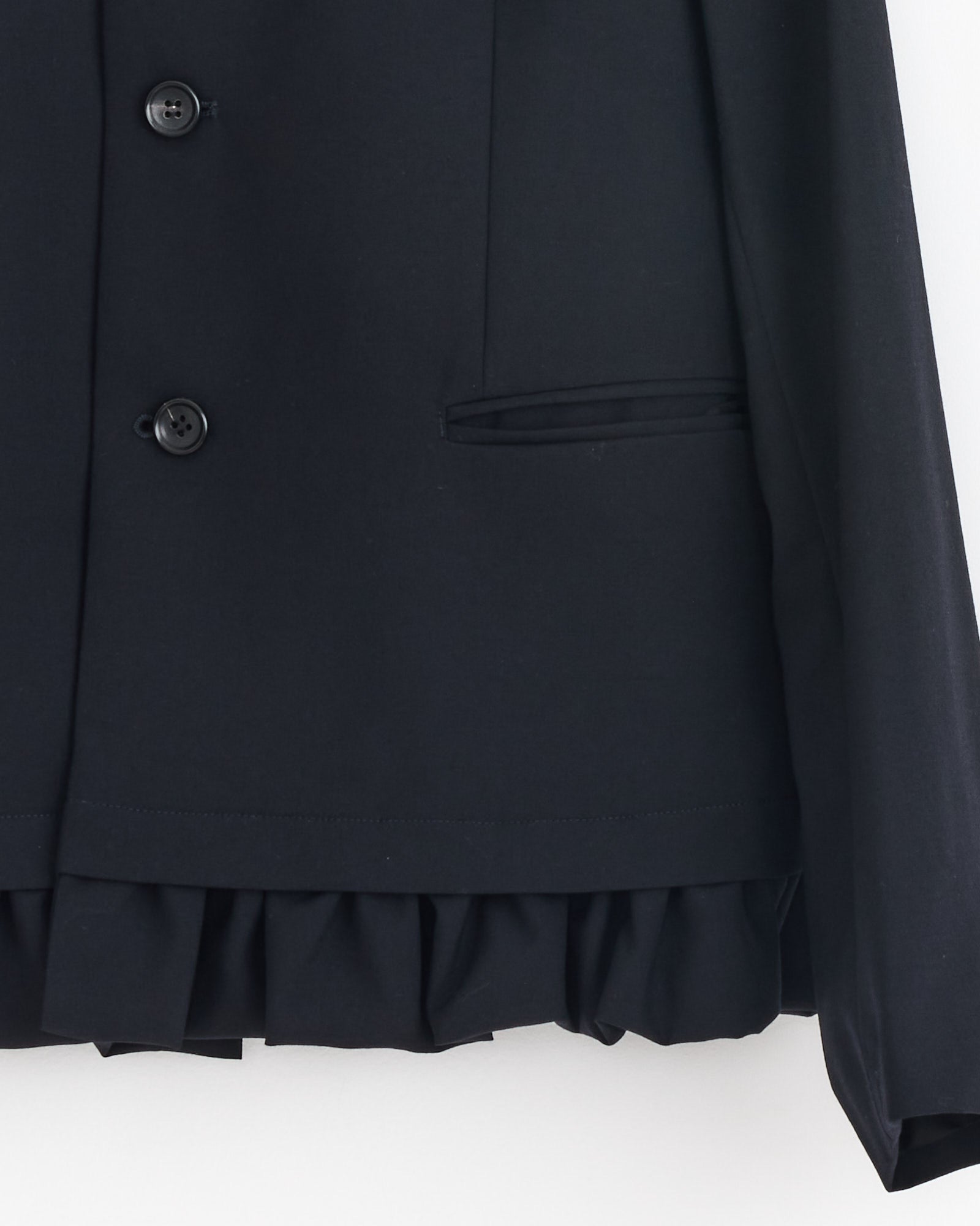 Close-up of the Peter Pan Jacket in Navy by Comme Des Garçons Girl, featuring black buttons and a flap pocket. A ruffled hem peeks out beneath, adding a refined touch. Expertly crafted in Japan for superior quality.