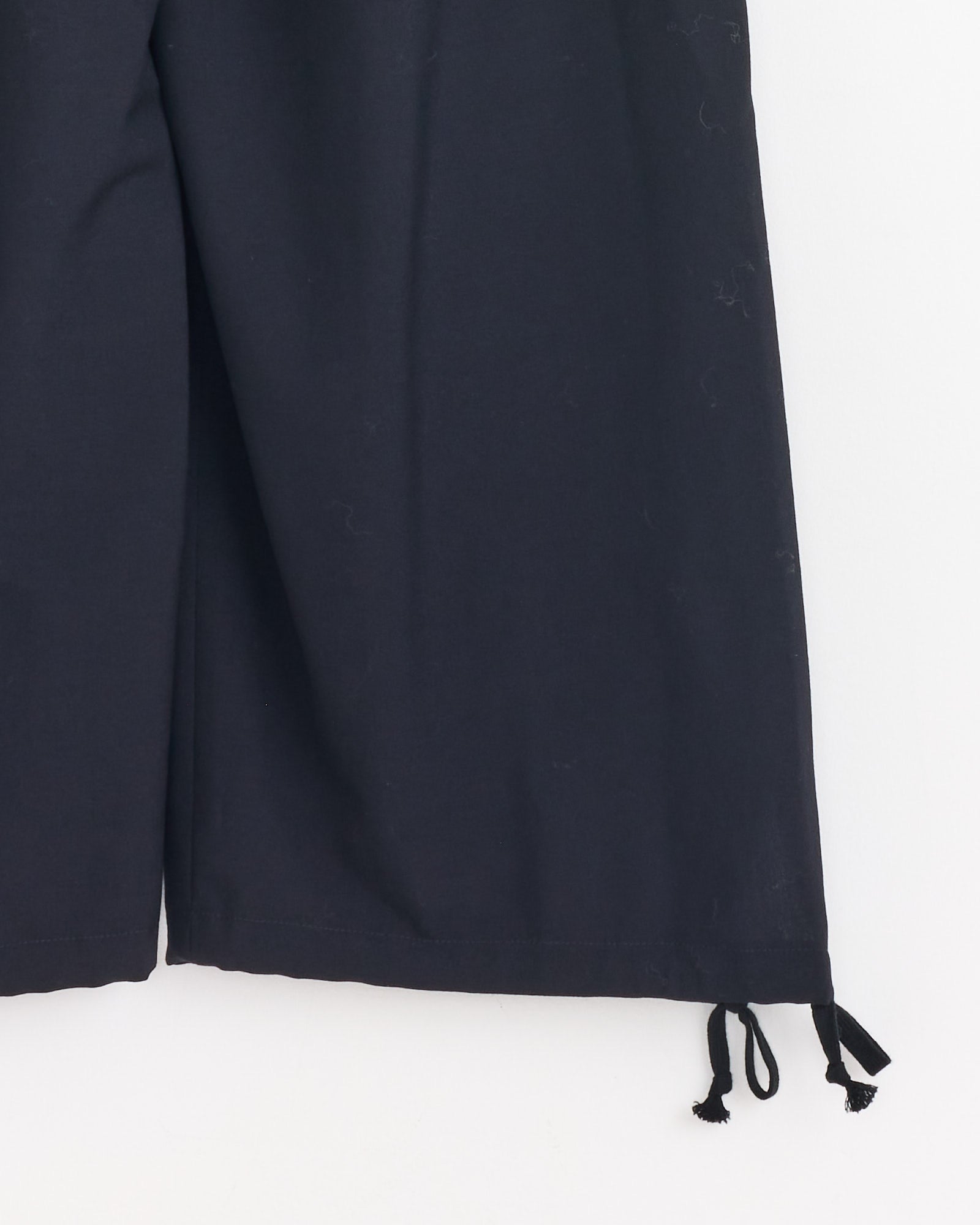 A close-up of the lower half of the Comme Des Garçons Girl Drawstring Cuff Pant in Navy, featuring wide legs and drawstring hems, set against a white background.