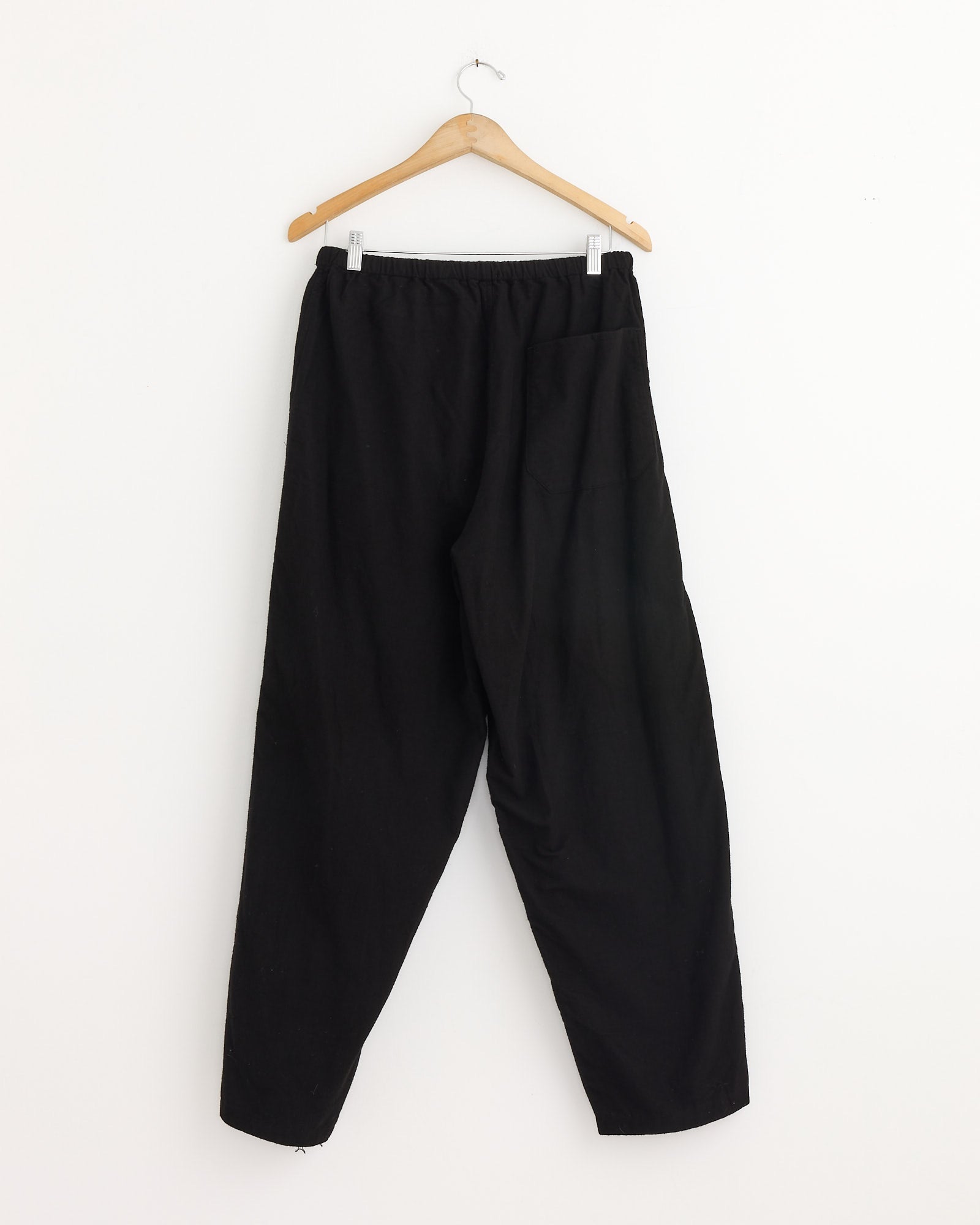 The Comoli Flannel Tapered Pant in Black, made in Japan from soft cotton flannel, is displayed on a swinger.