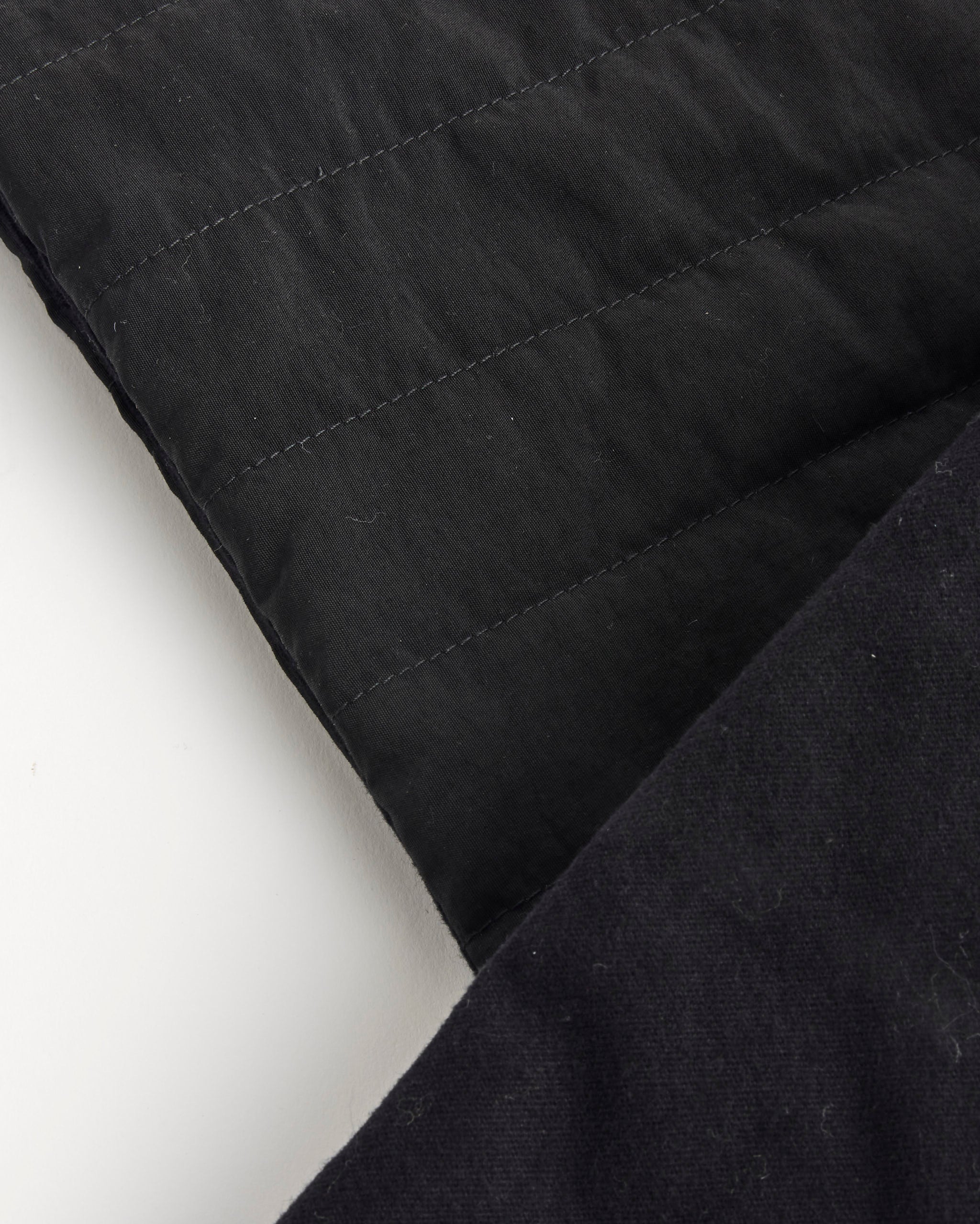 Close-up of two overlapping pieces of dark fabric from Clyde’s Puff Scarf on a white surface; one features visible horizontal stitching, while the other is smooth and plain—ideal for a stylish, reversible look.