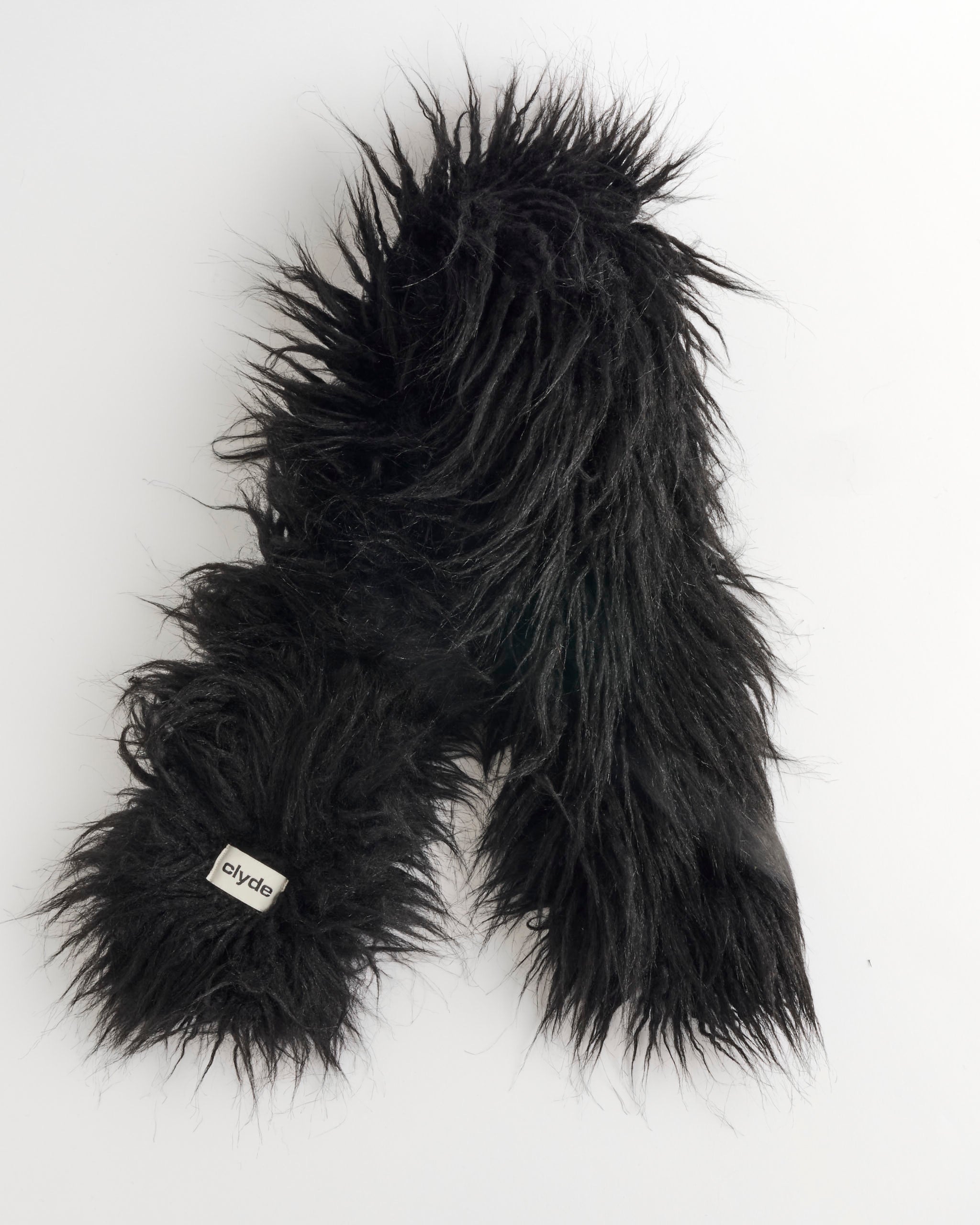 A black, long, shaggy faux fur unisex Sue Scarf by Clyde rests on a white background, featuring a small fabric tag labeled "Clyde.