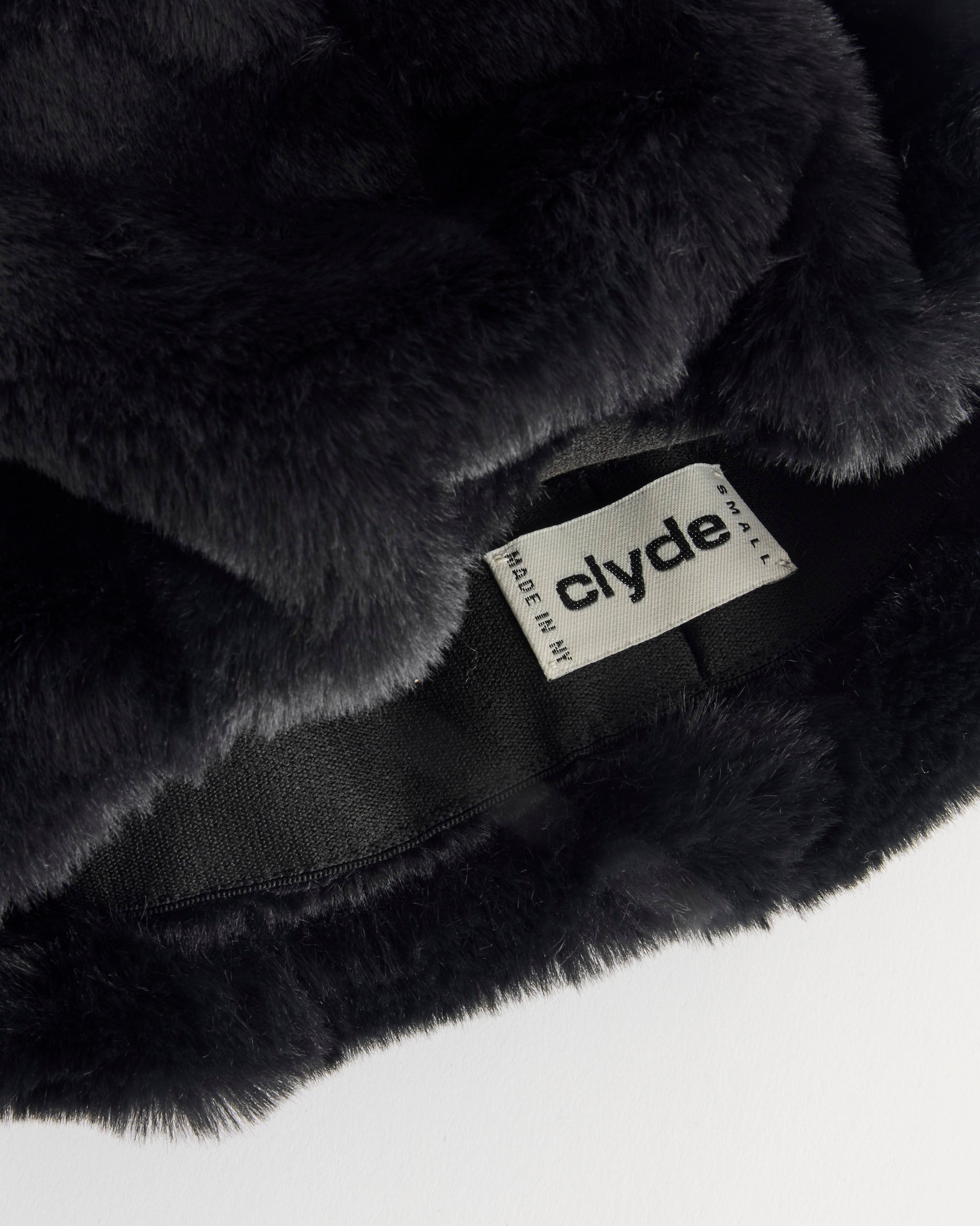 Close-up of the Clyde Faux Fur Beret in Black, featuring a visible white tag with “Clyde” and “MADE IN NY” in black text. The unisex beret is shown on a white surface.