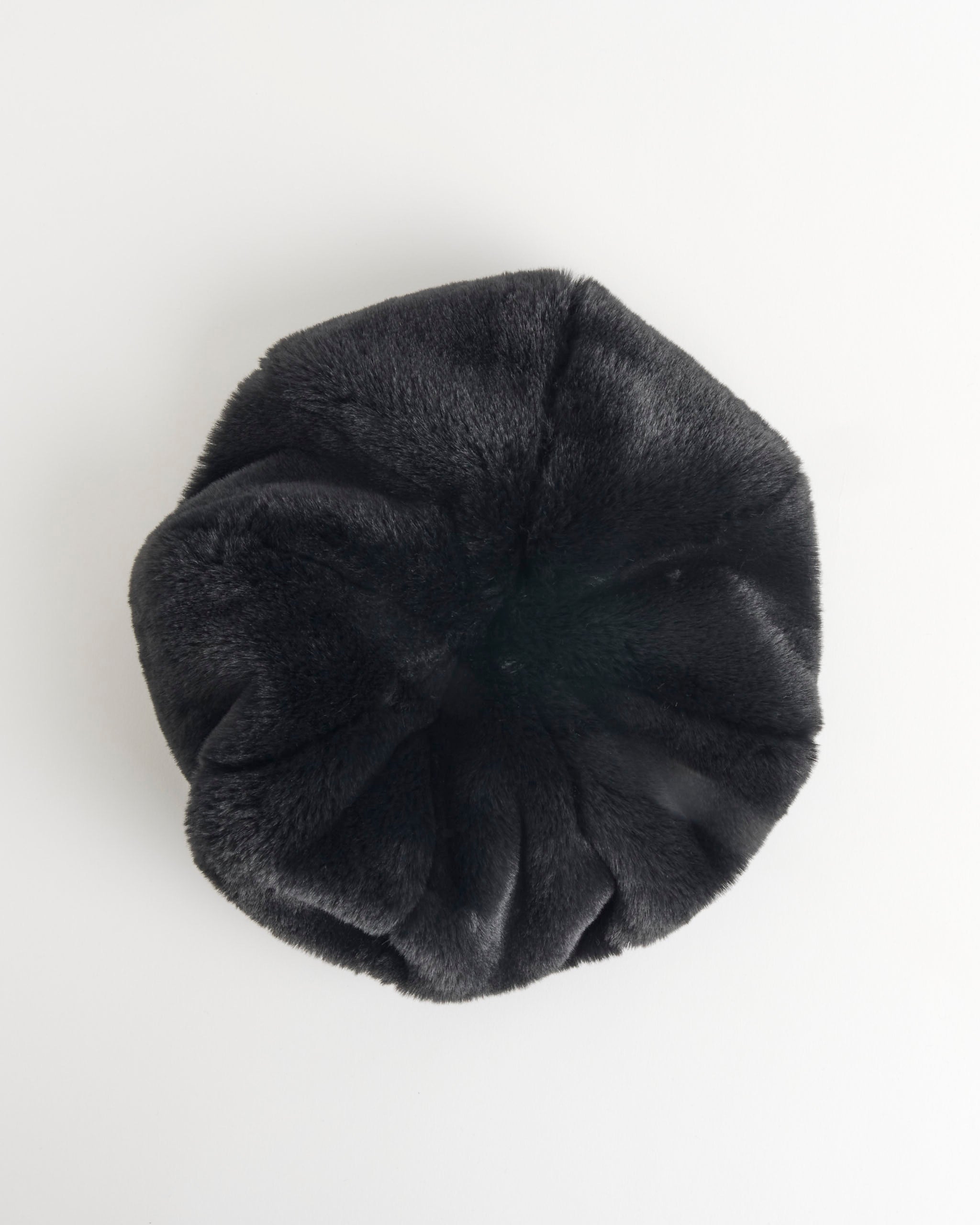The Clyde Faux Fur Beret in Black is shown from above on a plain white background, highlighting its round shape, soft velvety texture, and gathered center seams. This unisex accessory offers a chic and cozy look.