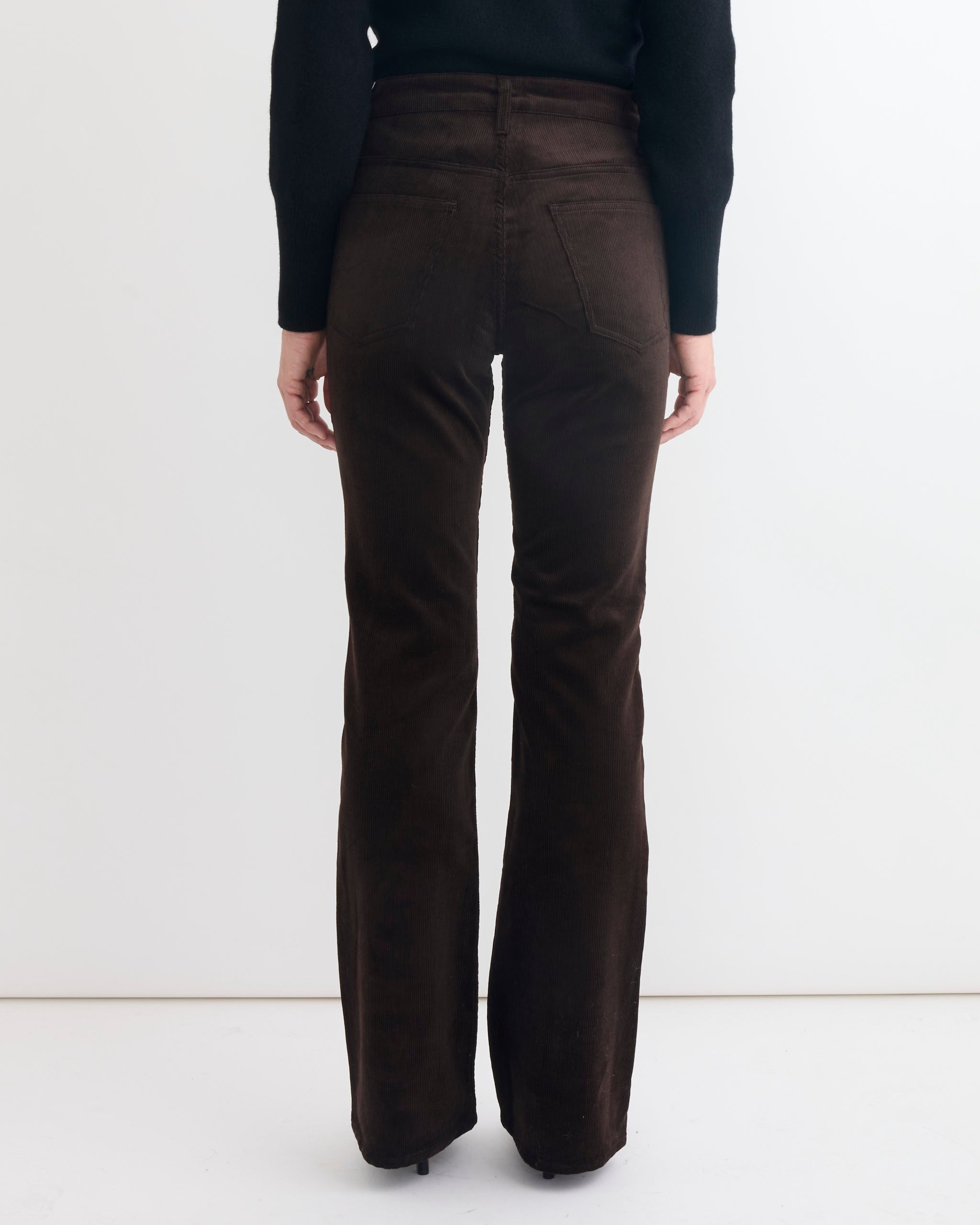 A person faces away from the camera, wearing Comoli’s Corduroy Pant in Brown and a black long-sleeved top, set against a plain white background.