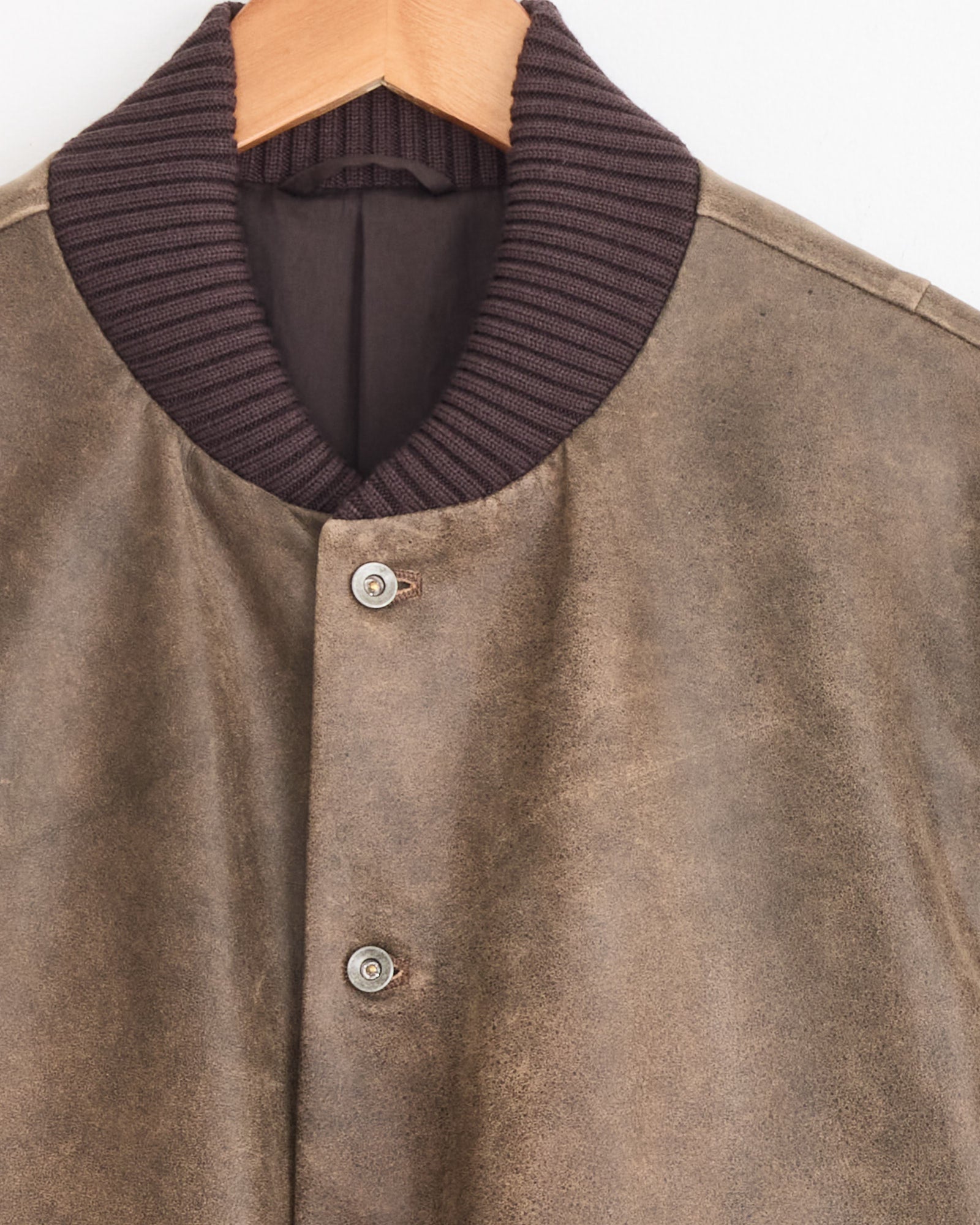 A close-up of the Cale Antique Calf Jacket in Brown on a wooden hanger, highlighting its ribbed dark brown collar and two metallic snap buttons. This stylish awards jacket is expertly crafted in Japan.