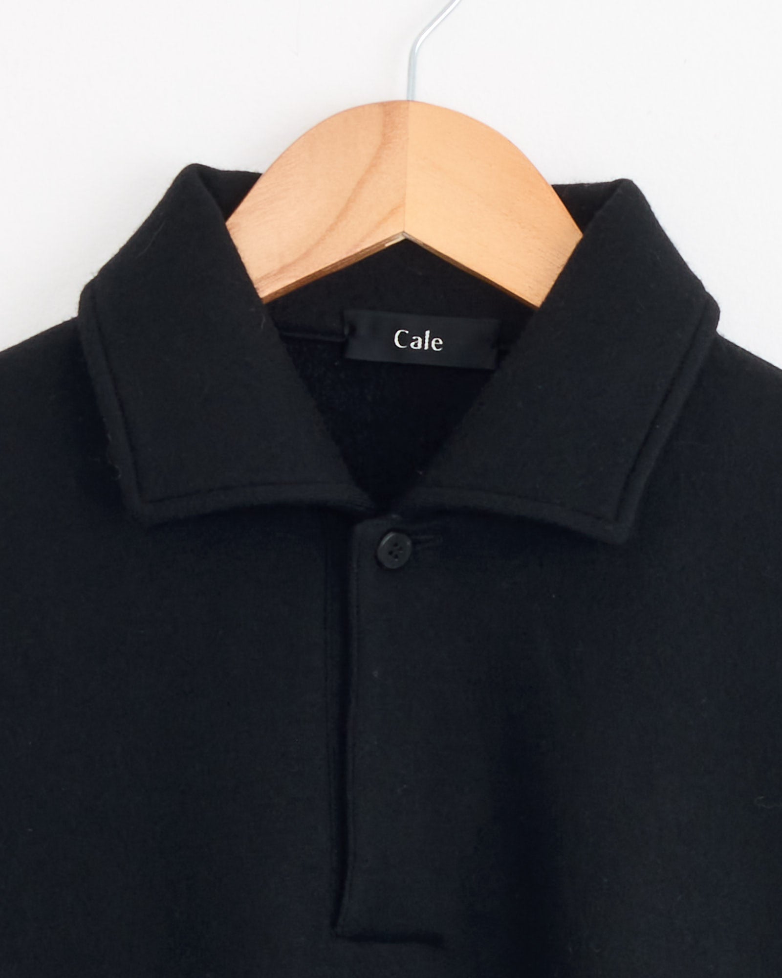 The Cale 120 Air Wool Fleece Polo in Black, featuring a single top button and crafted from Super 120's wool, is shown on a wooden hanger against a white background.