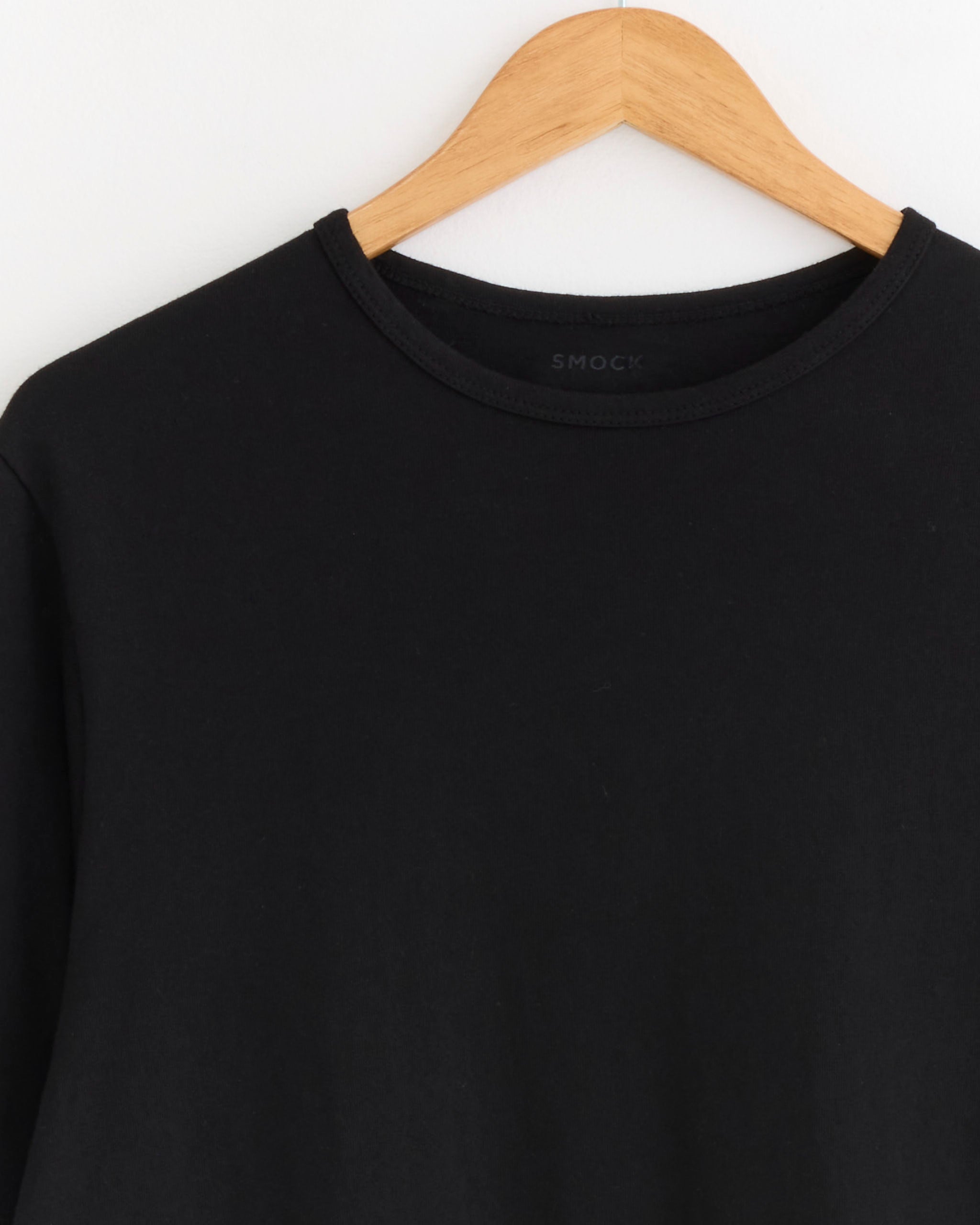The SMOCK Under Tee in Black, a classic crew neck combed cotton t-shirt, is shown on a wooden hanger against a white background.