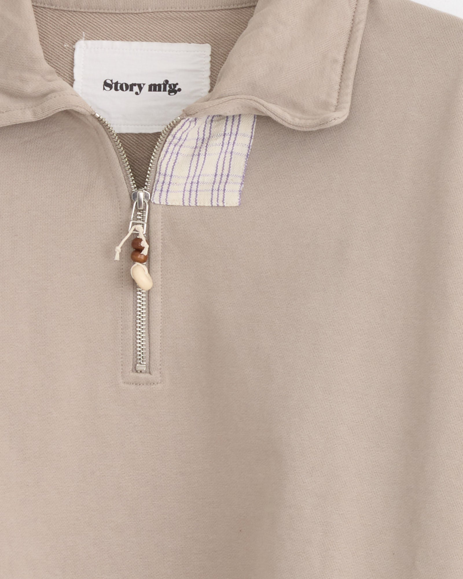 Close-up of the Story mfg Geo Pullover in Grey Picnic, an organic cotton sweatshirt with a partly open zipper, beaded pull, turned-down collar, boxy vintage fit, and brand label inside the neckline.