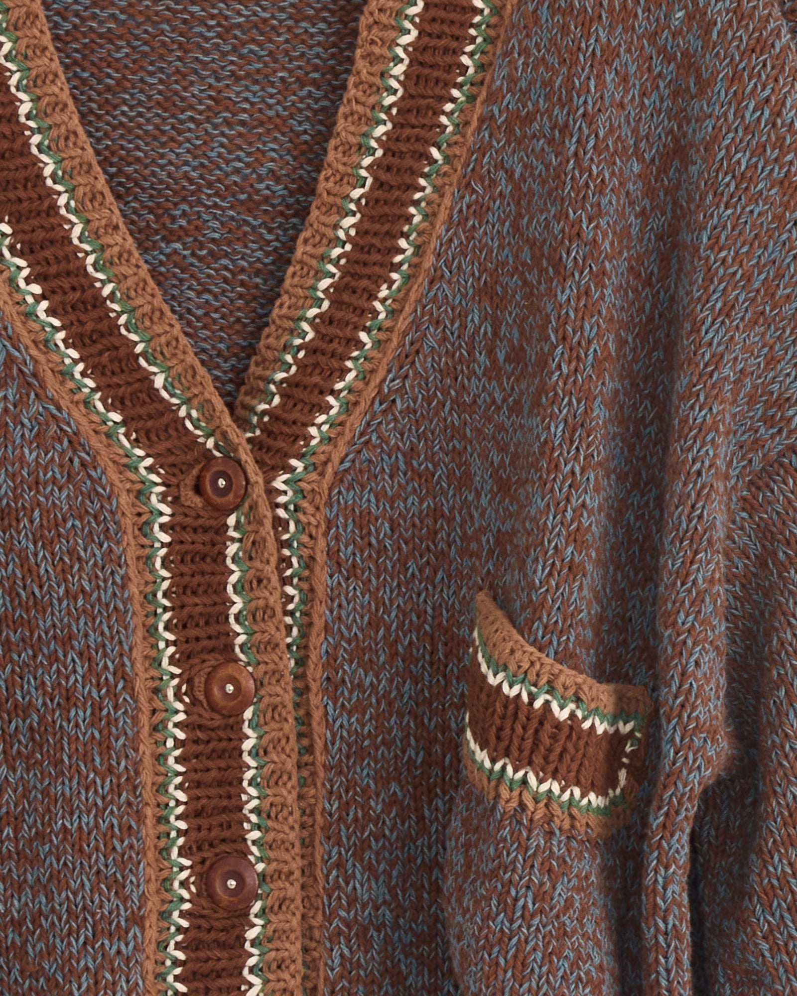 Close-up of the Story mfg Bulb Cardigan in Twisted Dusk—hand knit from organic cotton in brown and blue with a V-neck, brown buttons, pocket with brown, cream, and green striped trim, and natural dyes along the neckline and pocket edge.