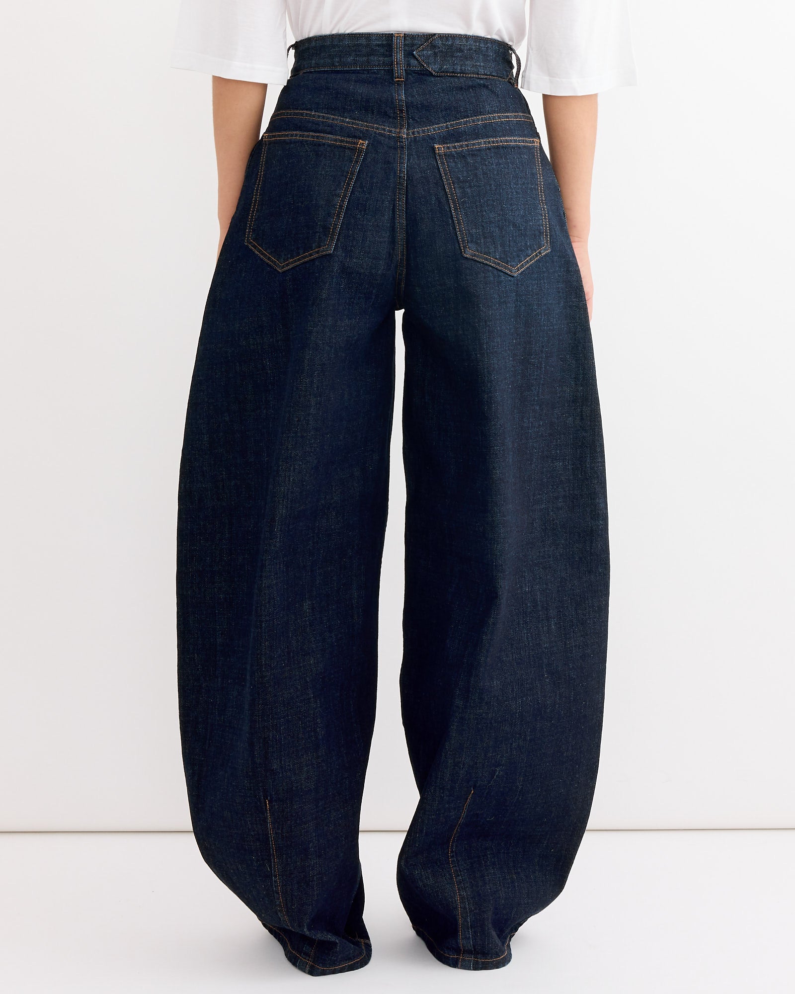 A person wearing Jacquemus Le De-Nimes Ovalo Pant in Dark Navy and a white shirt is shown from the back against a plain background to highlight fit. Contact us via online chat if you have any questions.