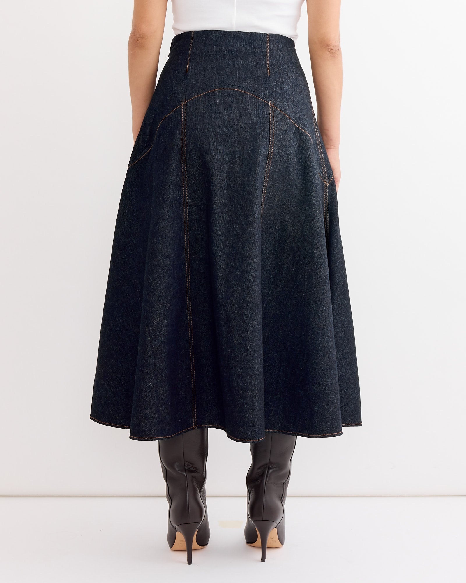 A woman wears the Jacquemus La Jupe Triangle De-Nimes Skirt in Dark Navy with boots, highlighting its perfect fit—great for those looking for sizing tips or online chat support.