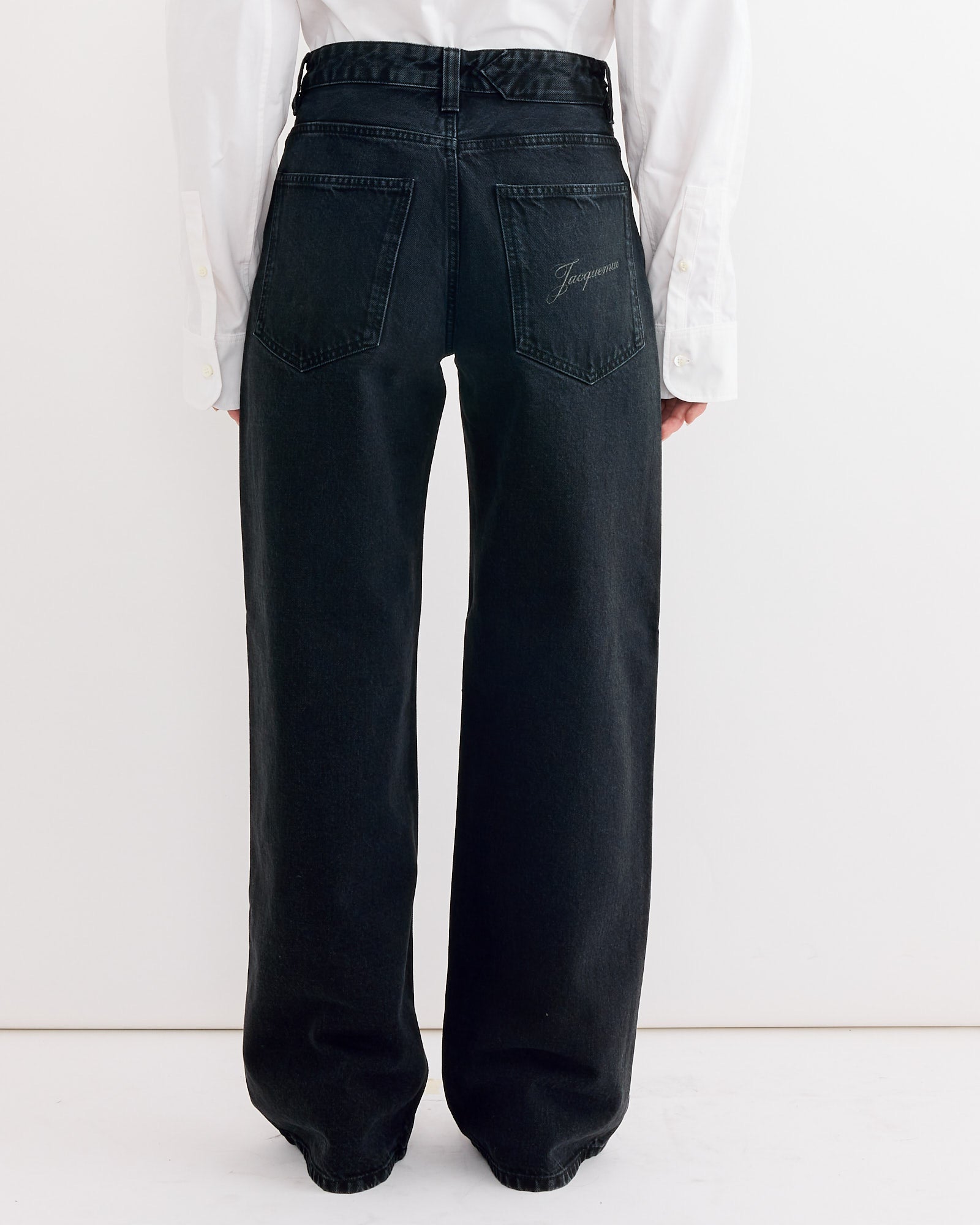 A person is shown from the back wearing Jacquemus Le De-Nimes Large Pant in Black and a white shirt, standing against a plain white background to showcase the relaxed, high-waisted fit for easy sizing reference.
