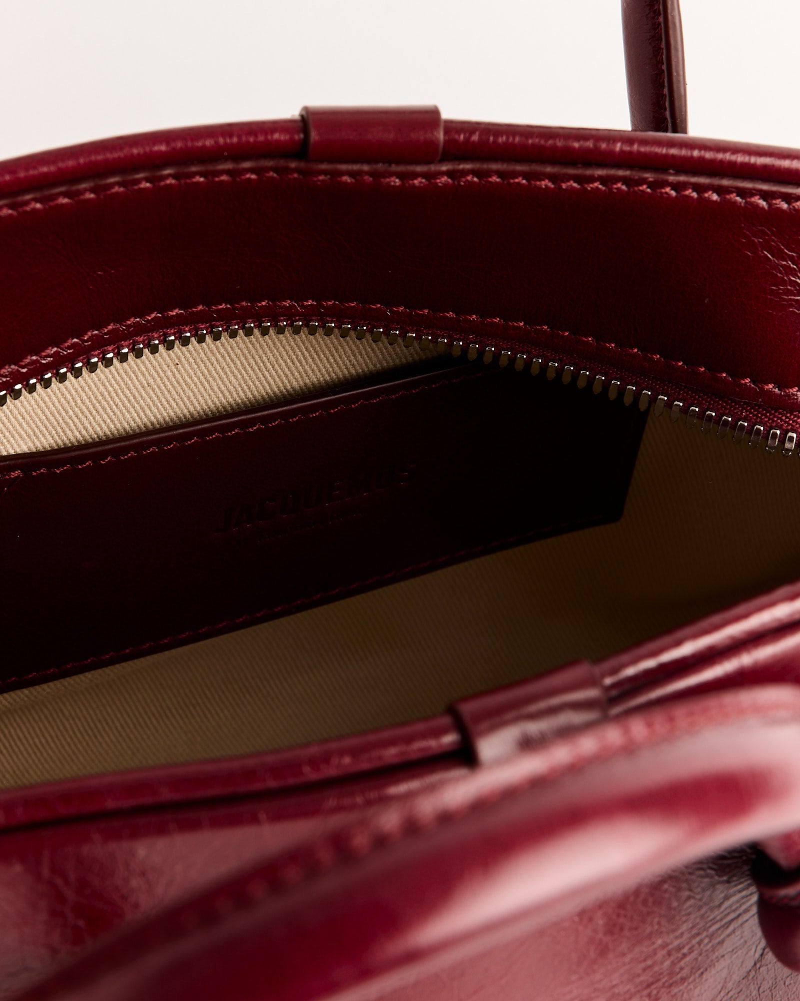 Close-up of the open top of the Jacquemus Le Petit Turismo Bag, made from burgundy vintage-finished leather, showing a beige fabric lining and an inner zippered pocket.